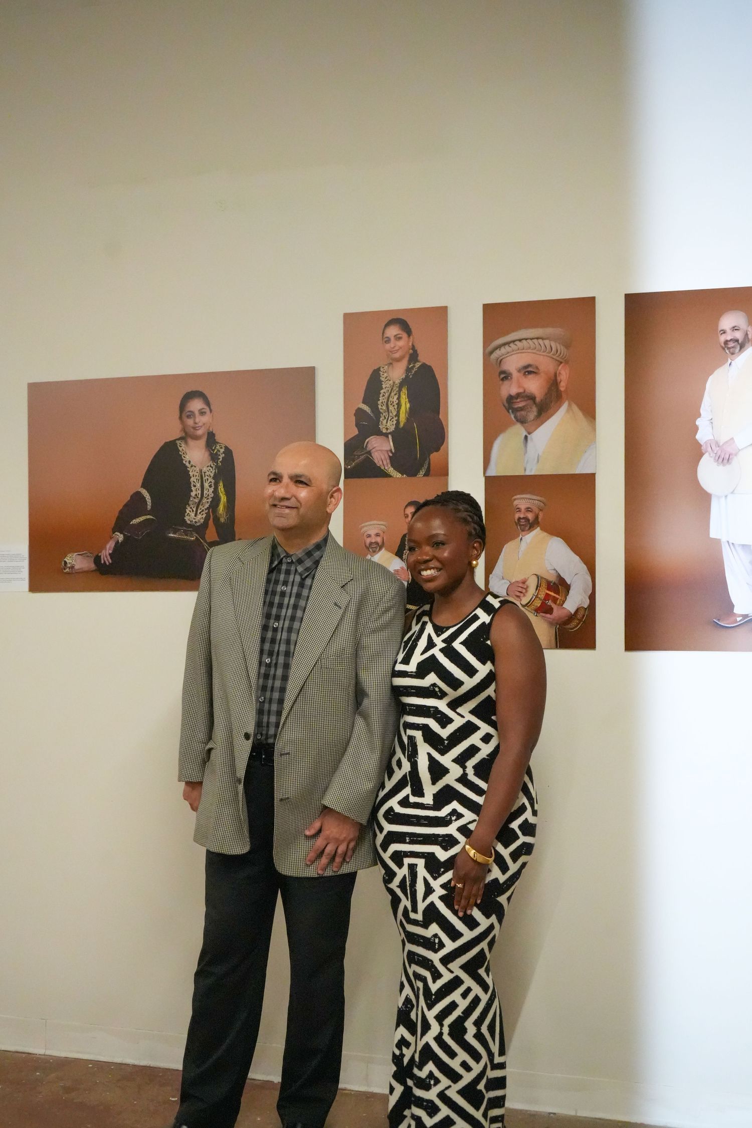 Two people posing together in front of portrait photography exhibition on a white gallery wall.