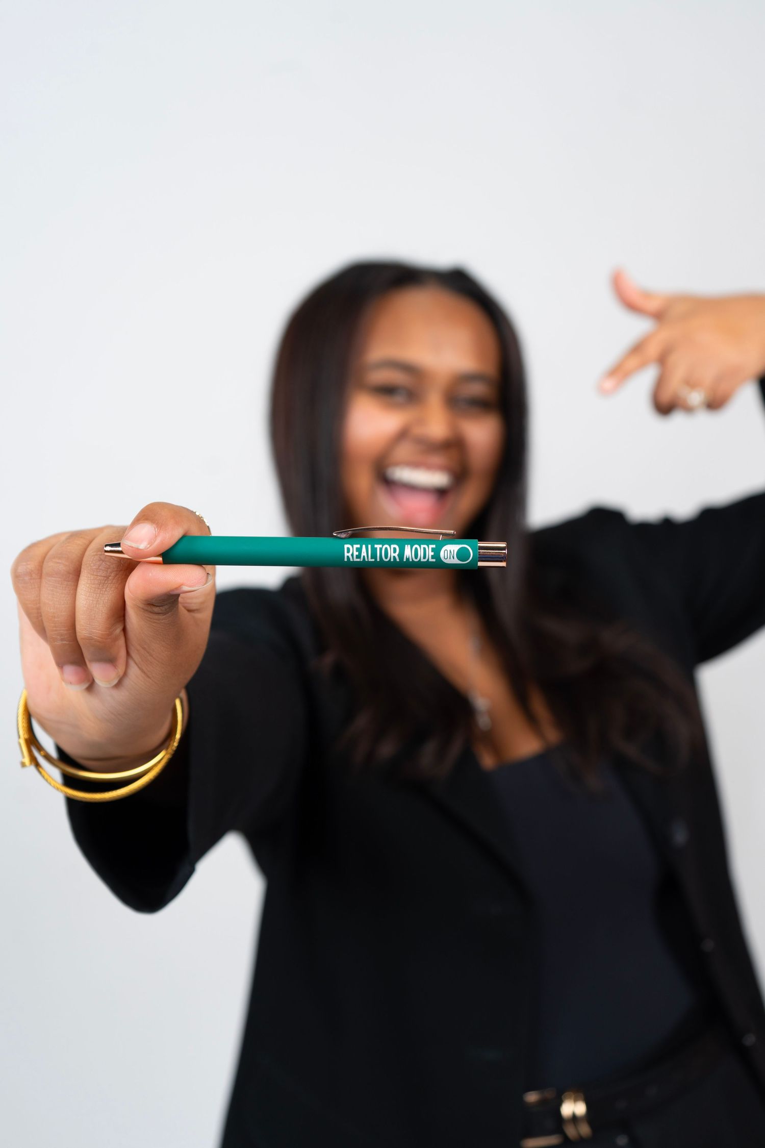 Smiling woman in black blazer holding a teal Realtor Code pen toward the camera.