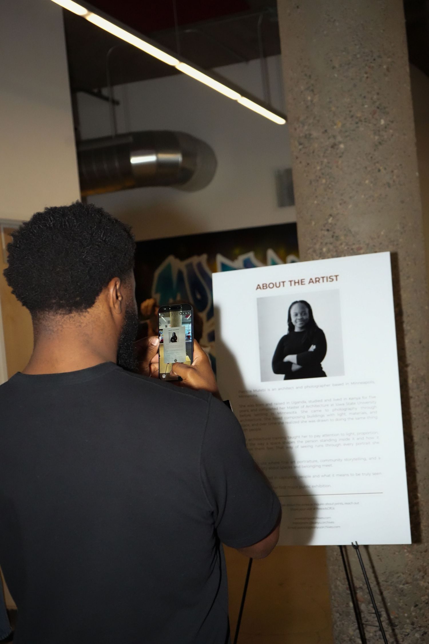 Man photographing an artist biography display board at an art exhibition with his smartphone.