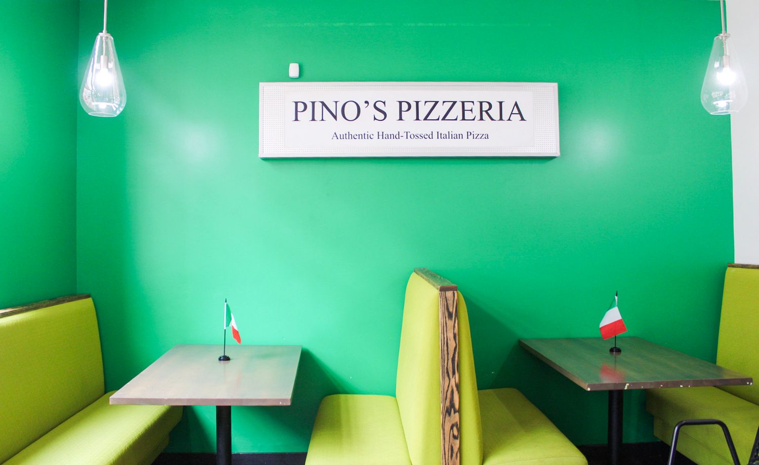 Pino's Pizzeria restaurant interior with bright green walls, yellow booths, and Italian flags on tables.