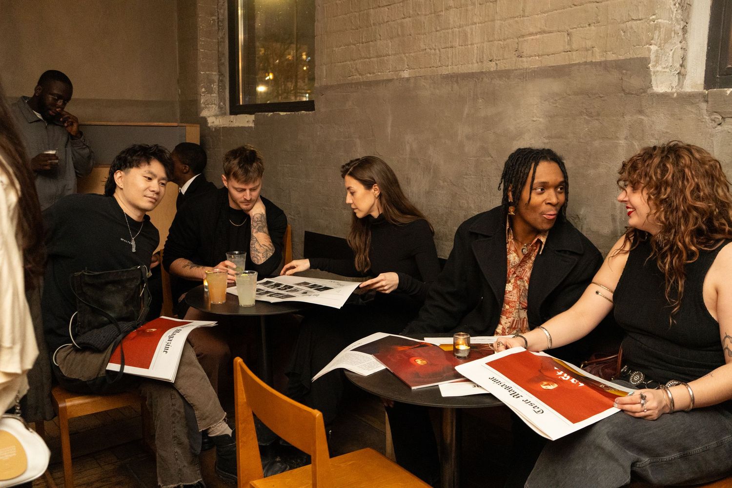 Group of young people sitting at a table in a cafe, reviewing printed materials together.