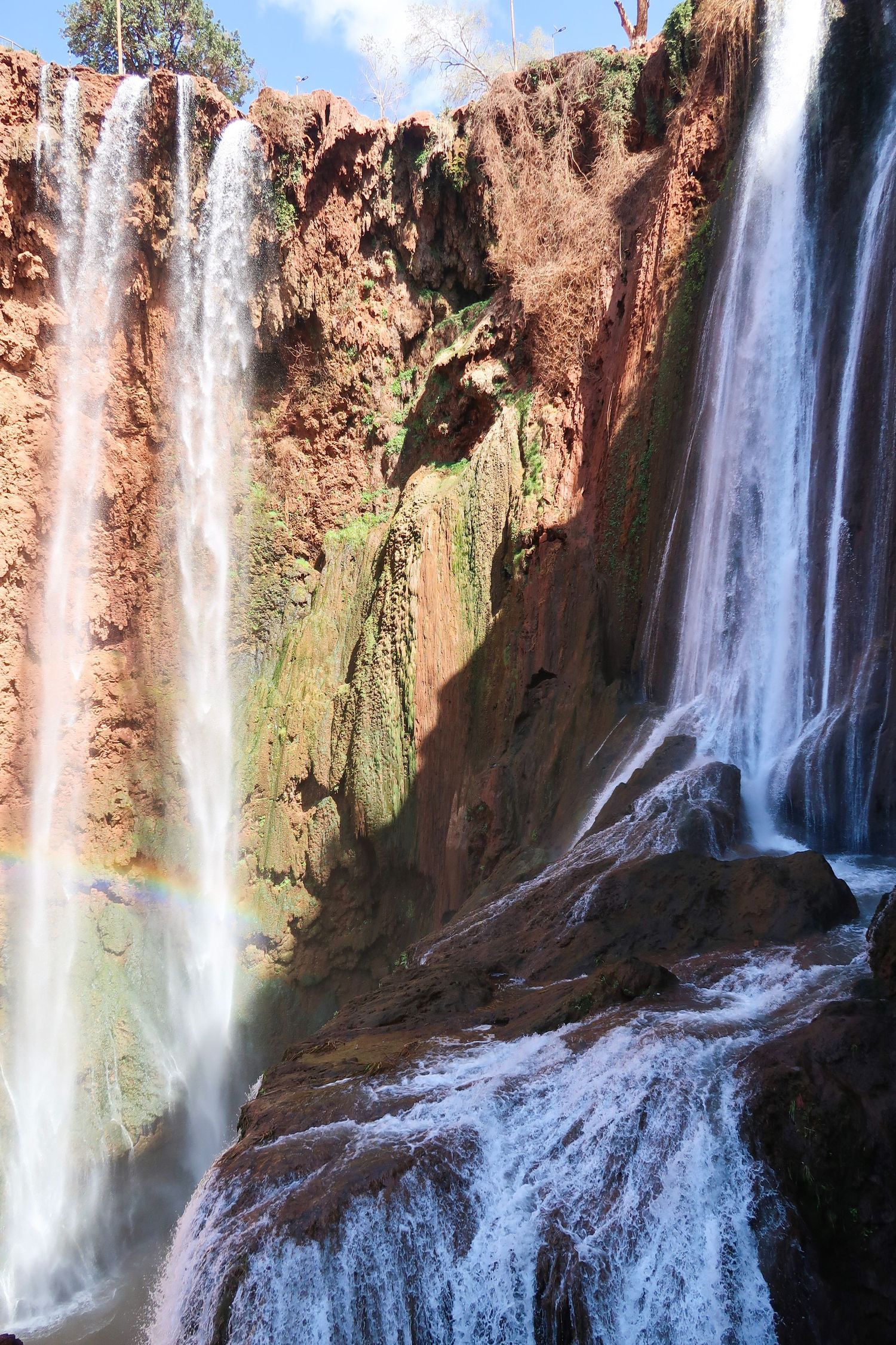 Multiple cascading waterfalls flowing over red rock cliffs in a natural landscape, ouzoud waterfall, morocco,  travel photography