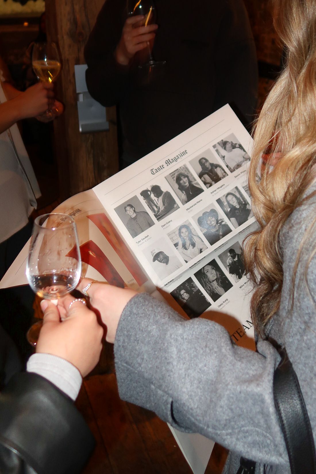 Woman holding wine glass and reading Taste Magazine at a social gathering event.