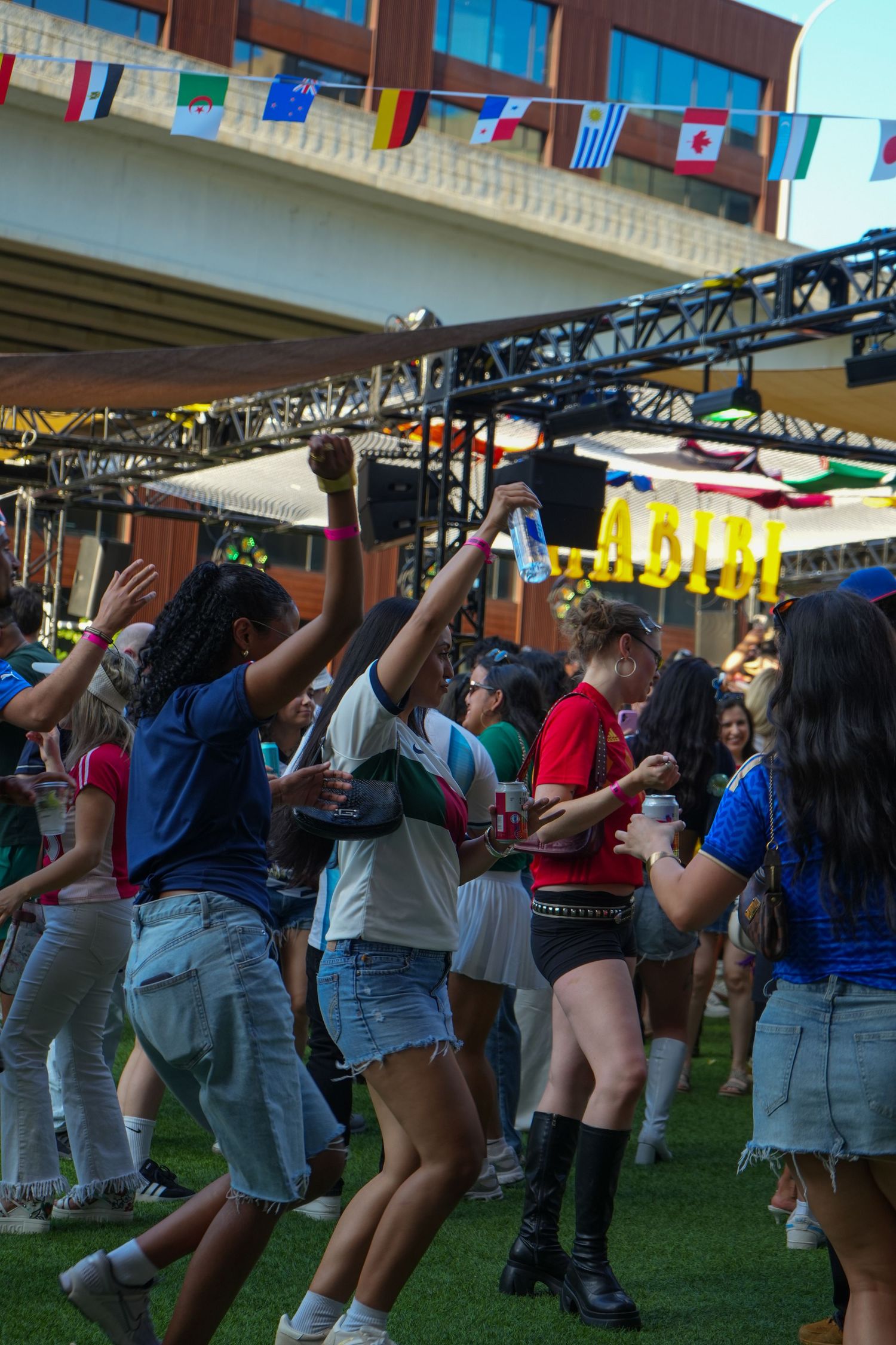Young people dancing outdoors at a festival with international flags and stage lighting.