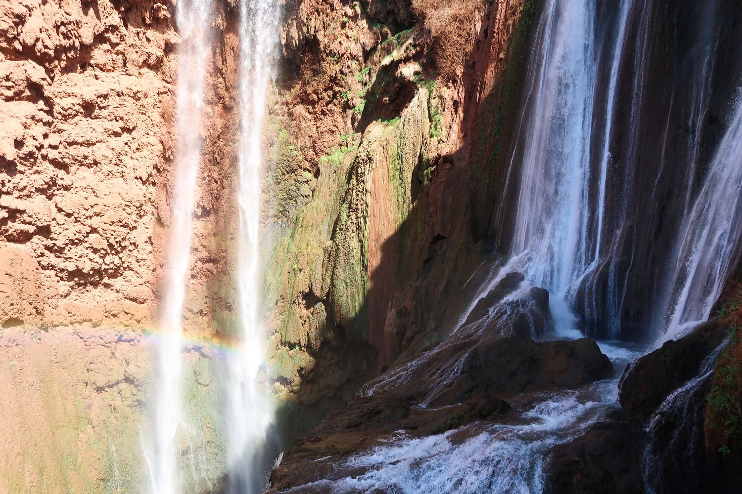 Scenic waterfall cascading down red rock cliffs in multiple streams against a natural canyon backdrop, travel photography, morocco