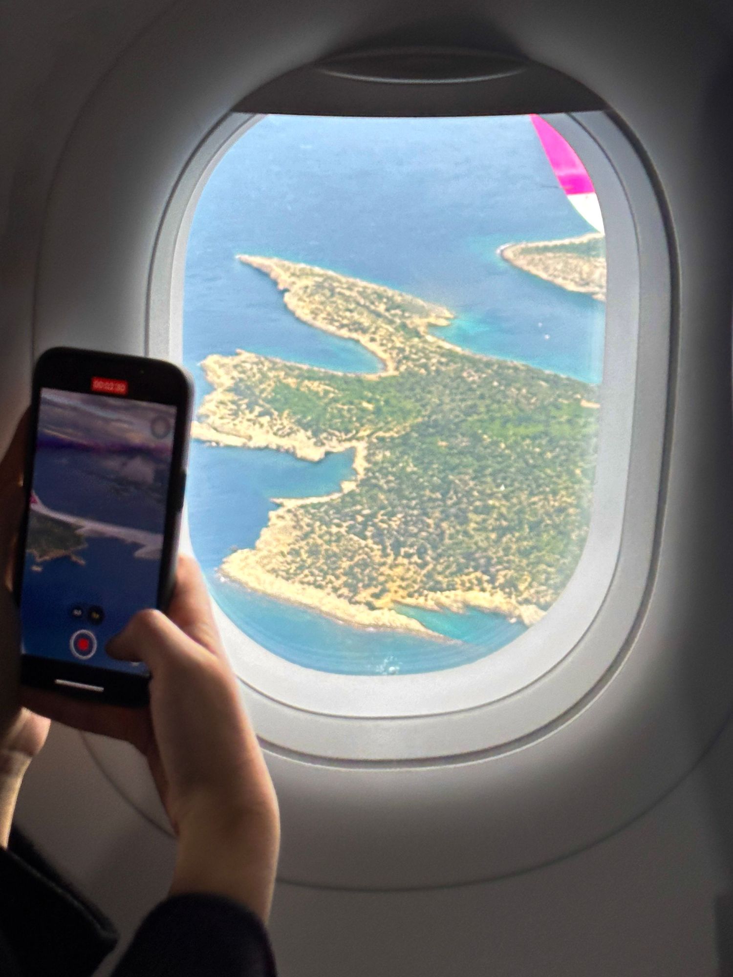 Aerial view of coastal islands through airplane window with phone camera visible, travel photography, ocean from airplane