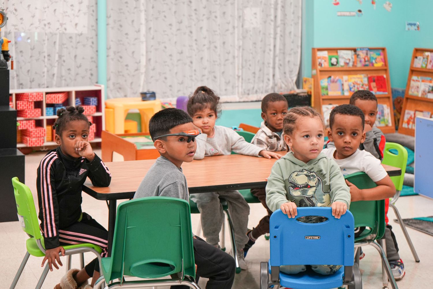 Young children sitting at a classroom table in a colorful preschool learning environment.