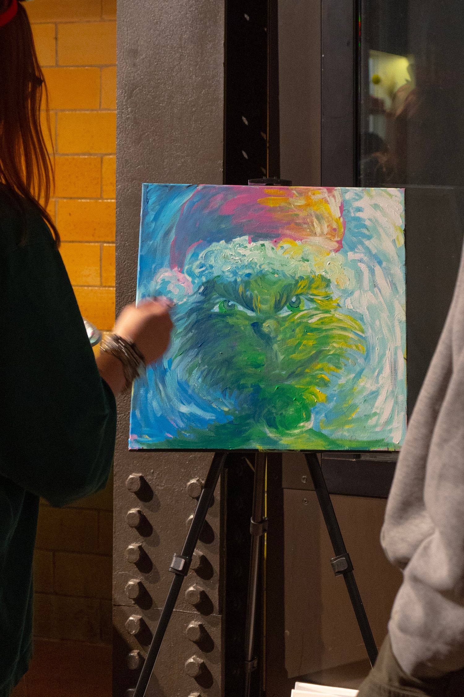 Artist displaying colorful abstract painting on easel with swirling blue, green, and pink tones in a gallery setting.