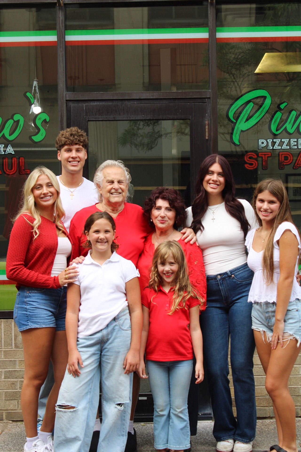 Family group photo smiling in front of Pino's Pizzeria restaurant, wearing red and white outfits.