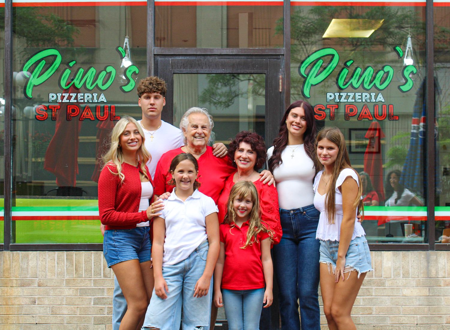 Family posing proudly in front of Pino's Pizzeria St. Paul restaurant entrance on a sunny day.