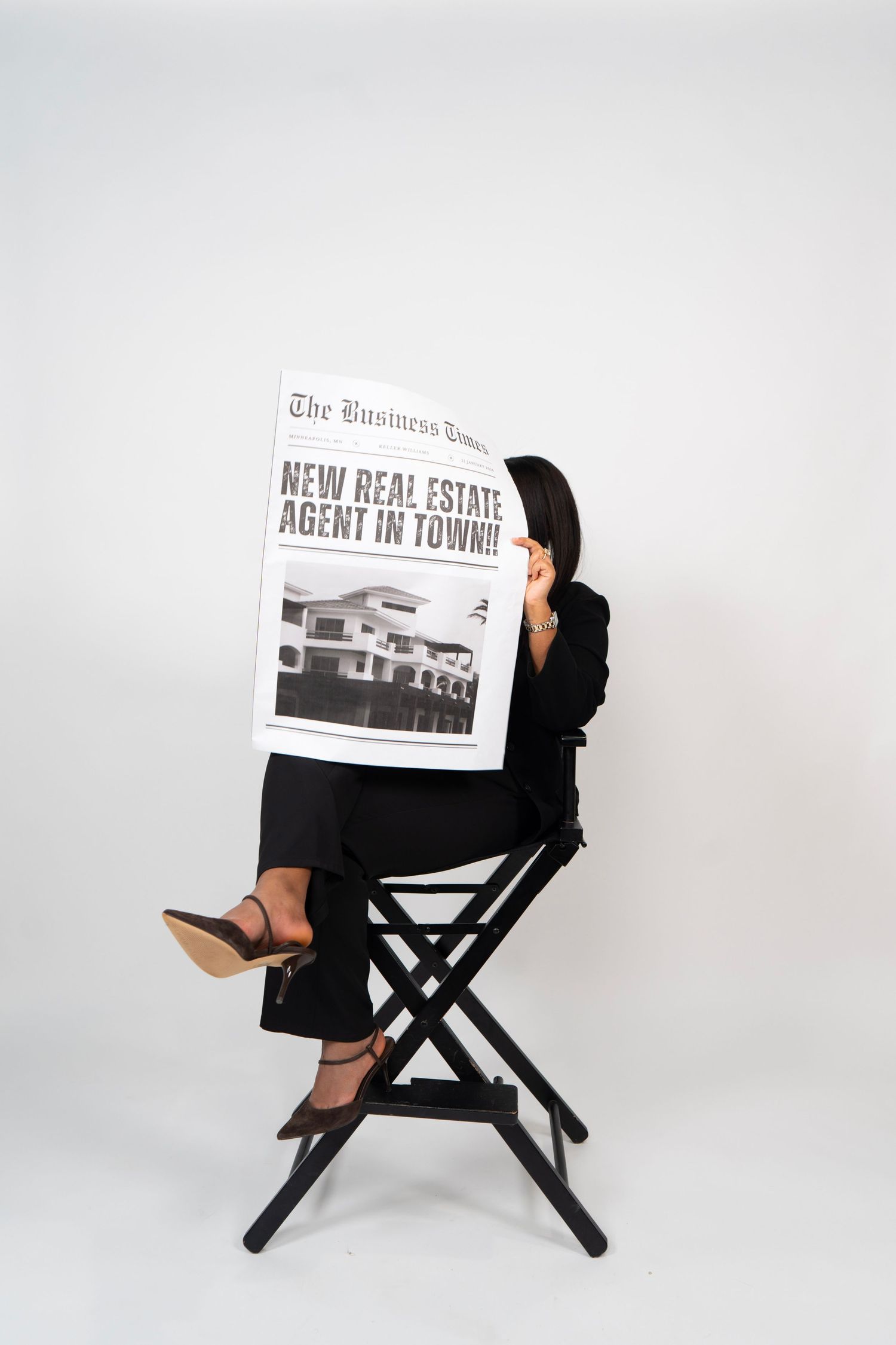 Woman in black suit sitting on director chair reading Business Times newspaper with headline New Real Estate Agent In Town.