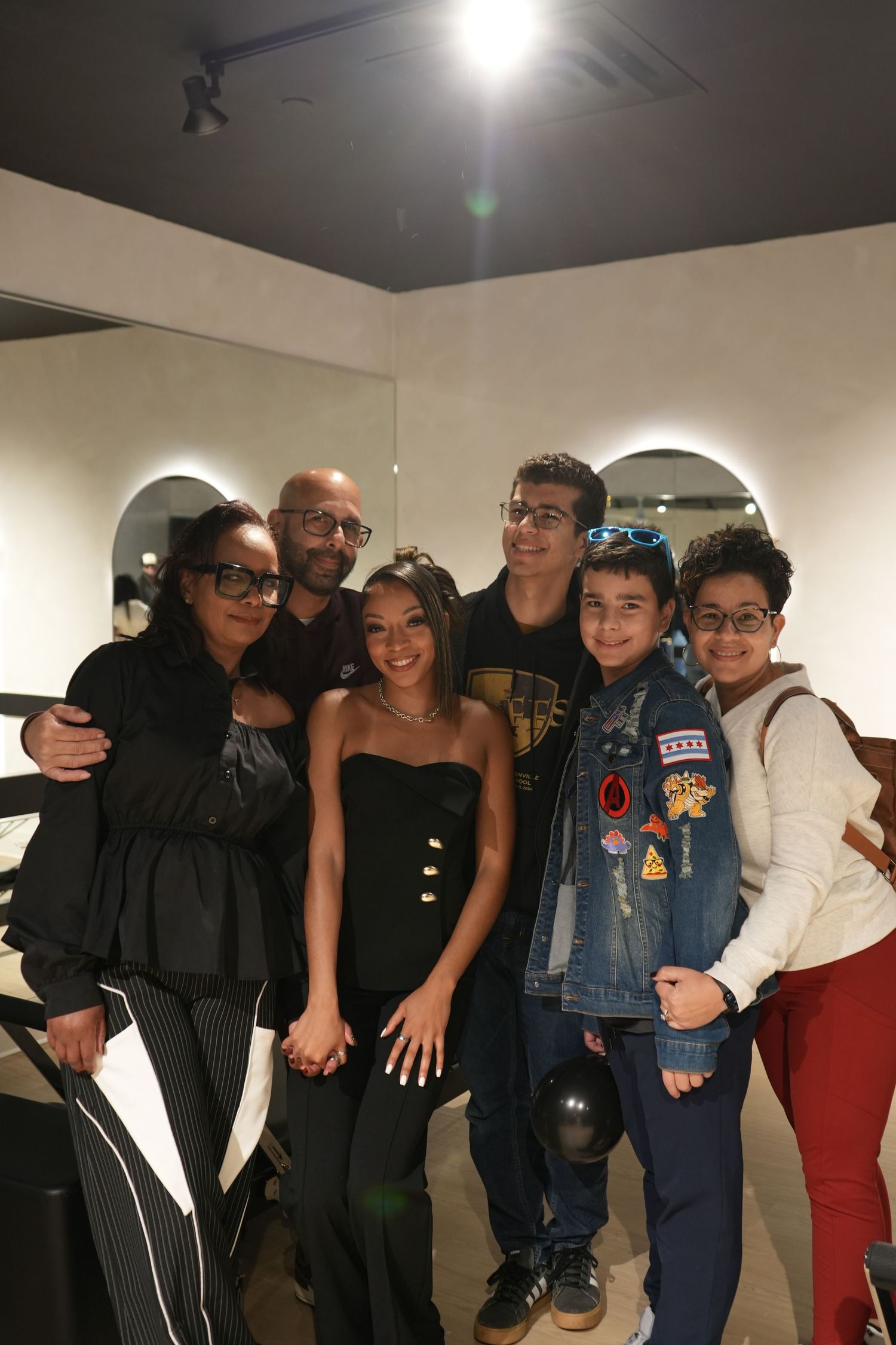 A group of six people posing together indoors, smiling for a photo in a modern room with arched decor.