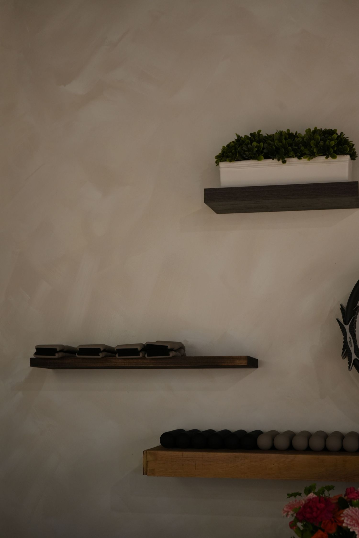 Three floating wall shelves displaying a green plant, candles, and folded textiles against a textured gray wall.