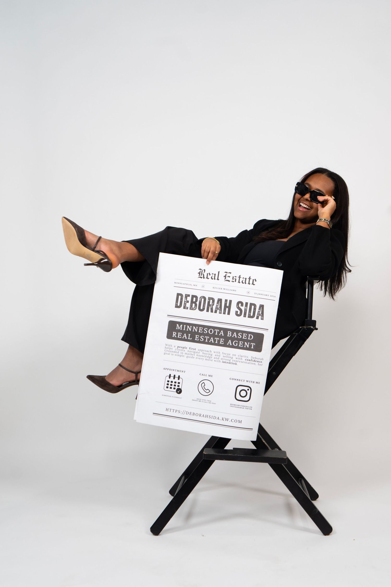 Deborah Sida, Minnesota-based real estate agent, poses confidently in a director's chair holding a promotional sign.