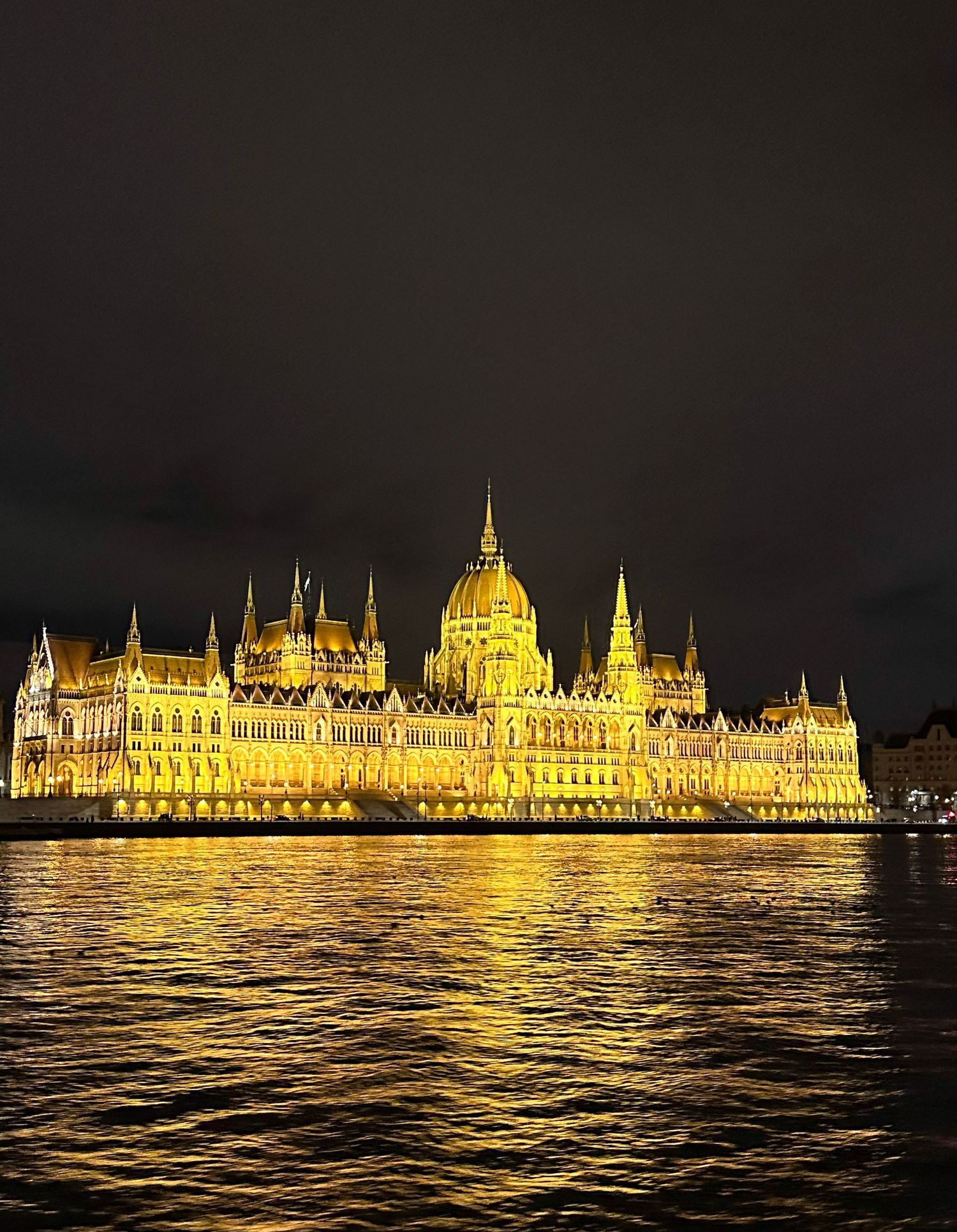 Hungarian Parliament Building illuminated in golden light at night, reflecting on the Danube River in Budapest.