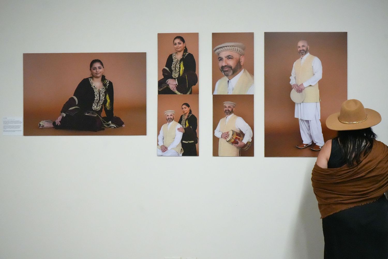 Person viewing gallery wall displaying six portrait photos of South Asian individuals in traditional cultural attire on brown background.