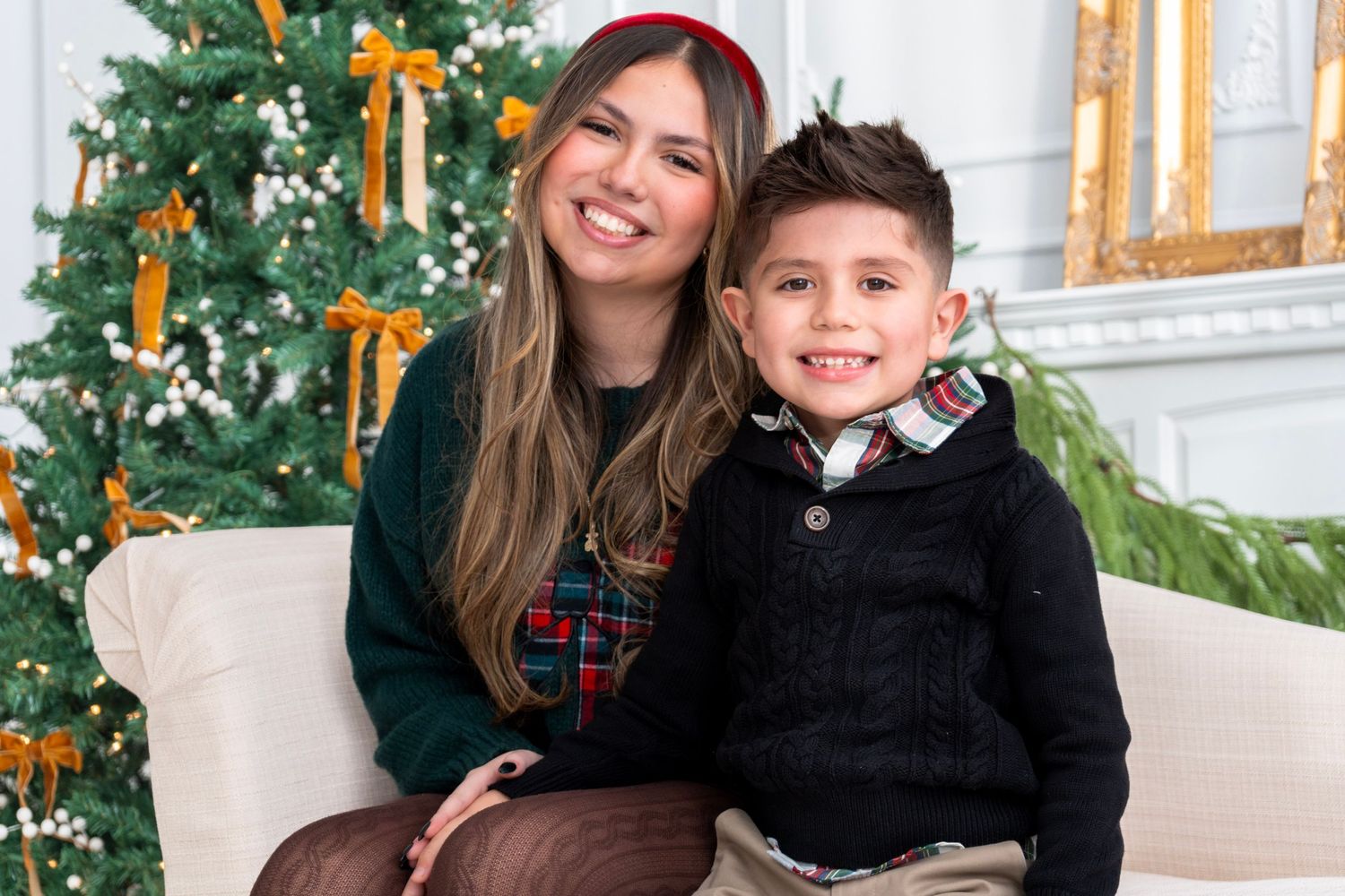 Woman and young boy smiling together in front of a decorated Christmas tree in a festive holiday setting.
