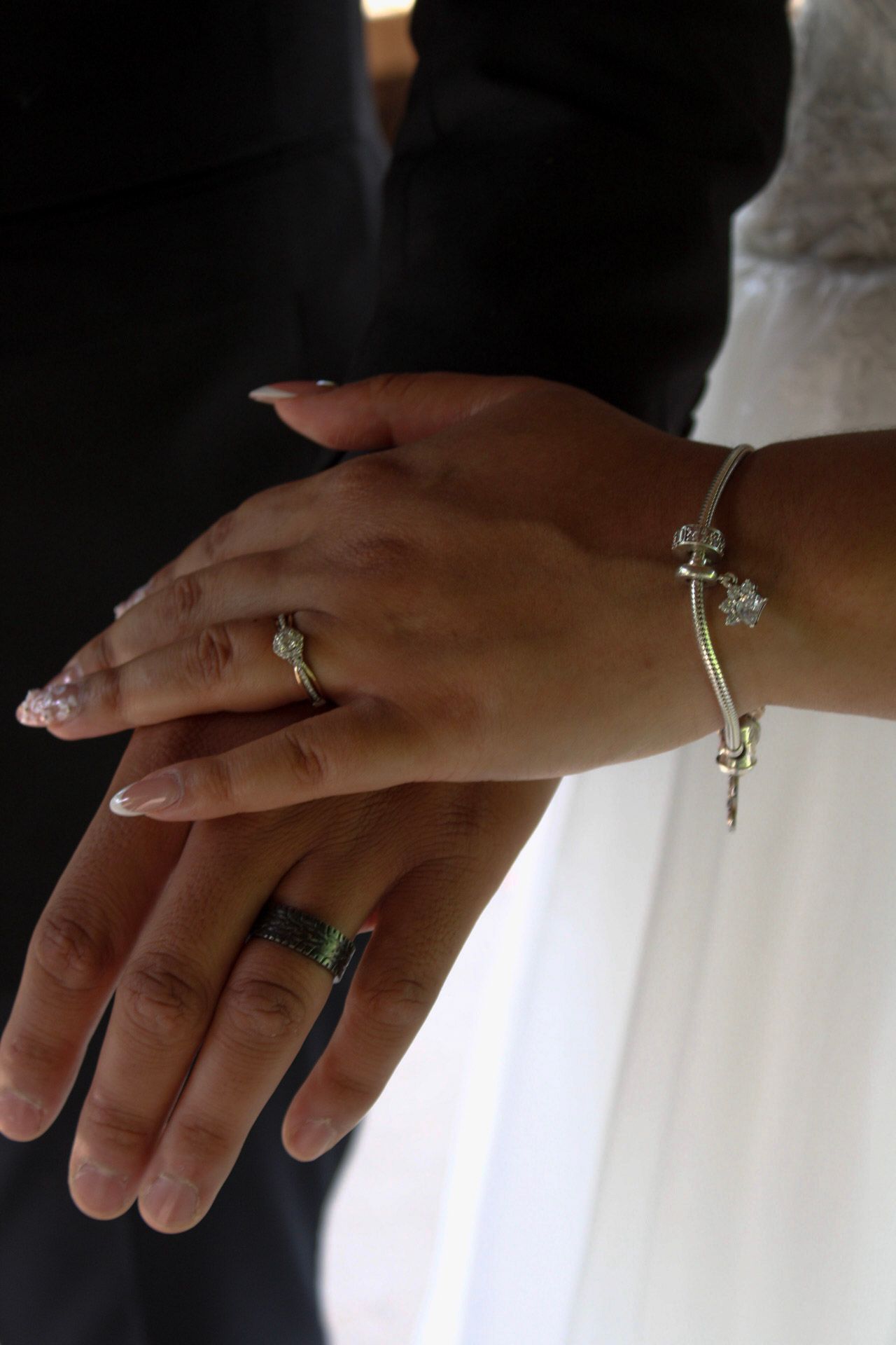Newlywed couple displaying wedding rings and diamond bracelet, bride wearing engagement ring with French manicure nails.