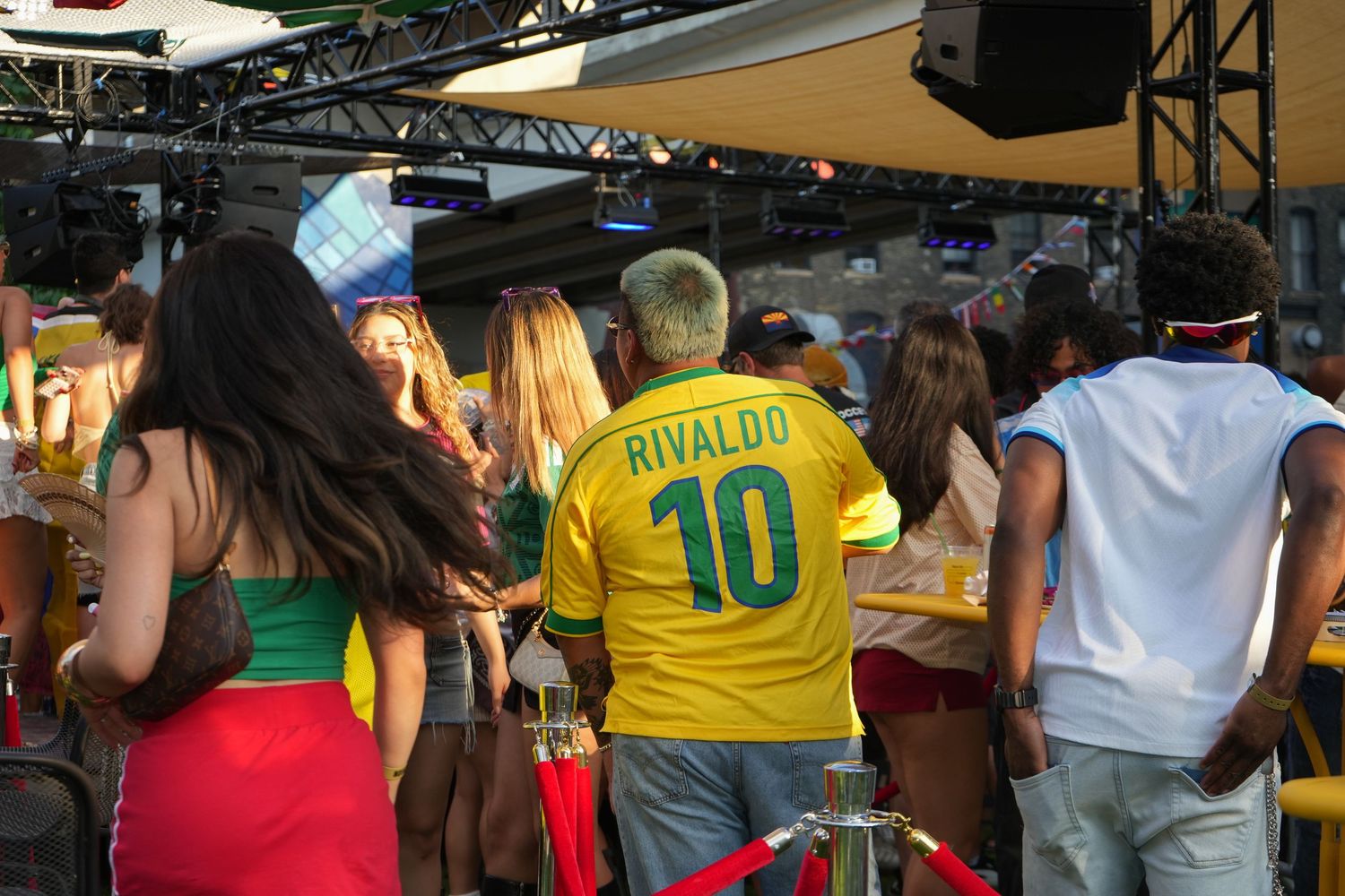 Man wearing Rivaldo number 10 Brazil soccer jersey at an outdoor sports bar gathering with fans.