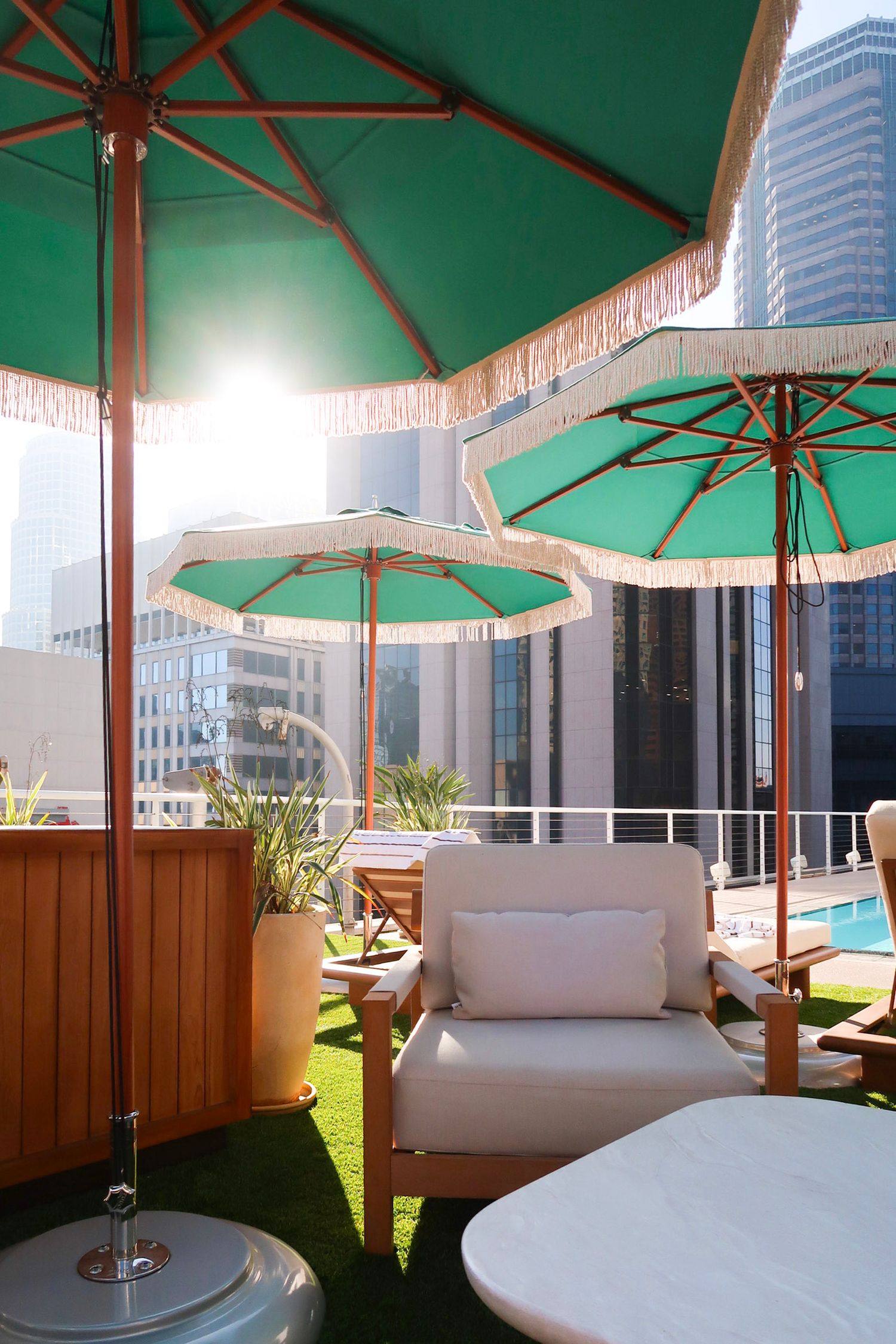 Luxury rooftop lounge area with green umbrella and white seating overlooking city buildings, travel photography, los angeles, rooftop pool