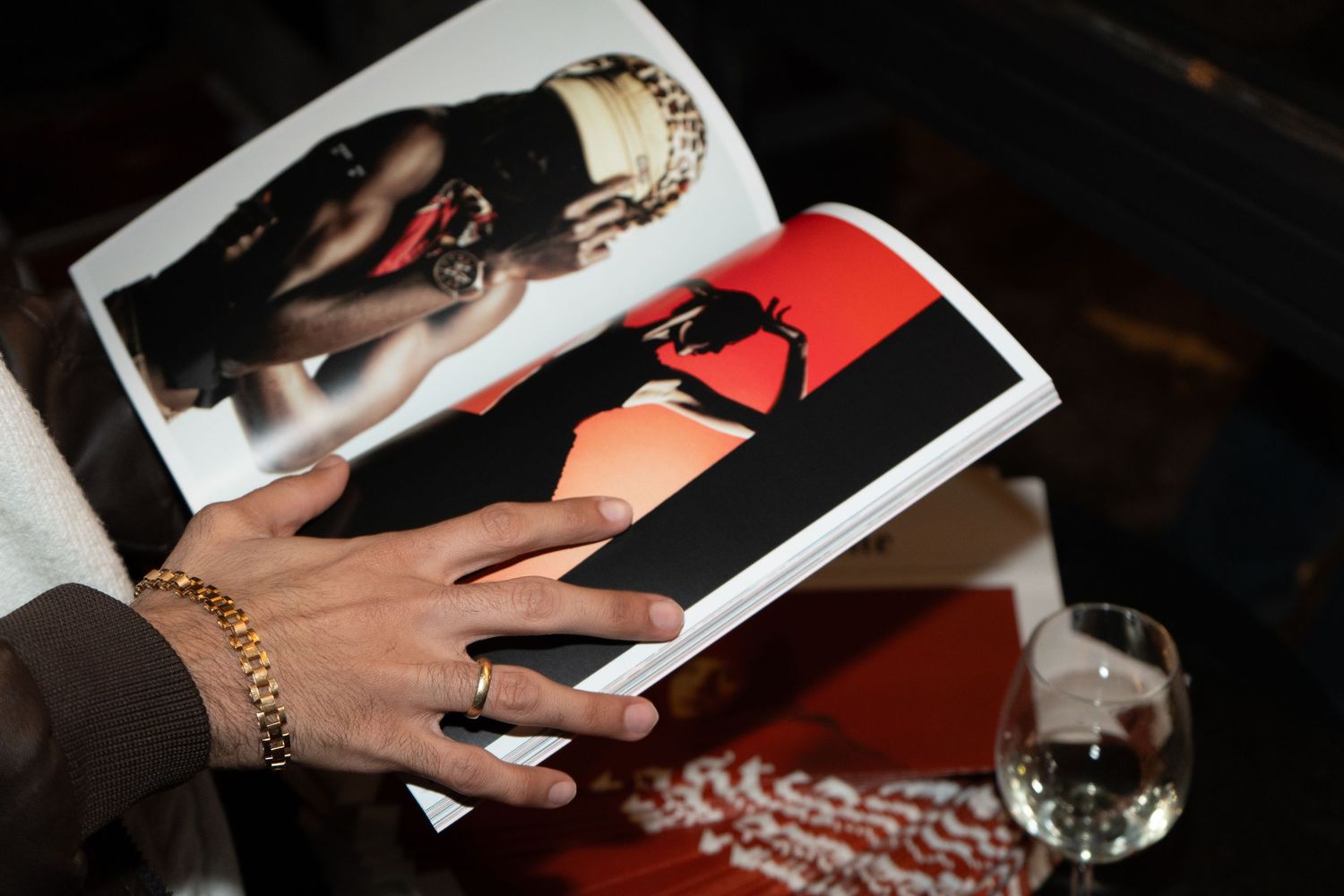 Person holding open magazine showing bold red and black fashion photography, with gold bracelet and ring visible.