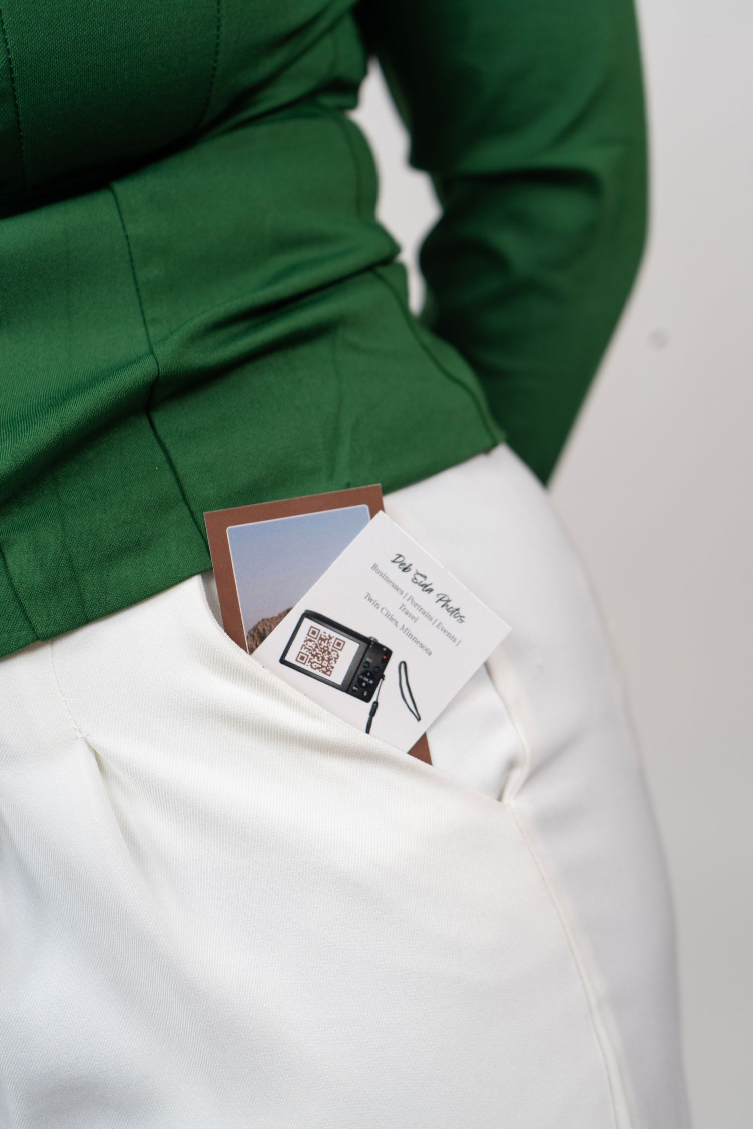 Person in green blazer and white pants with business card and photo in pocket.