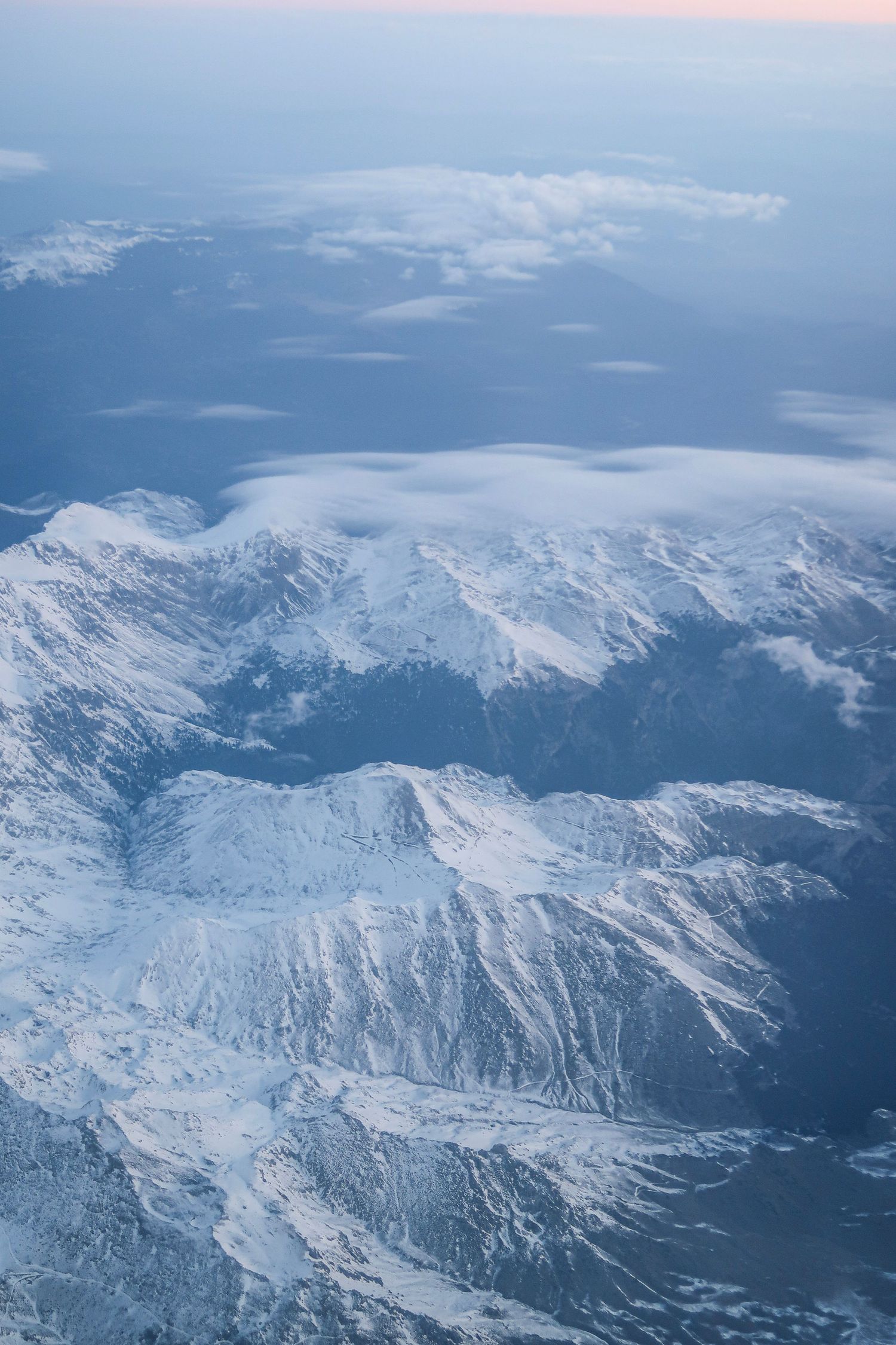 Aerial view of snow-covered mountain peaks and valleys under a blue winter sky, travel photography