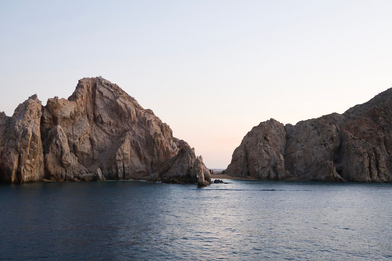 Rocky coastal cliffs rising from calm blue waters during sunset at Cabo San Lucas, travel photography, archs of cabo
