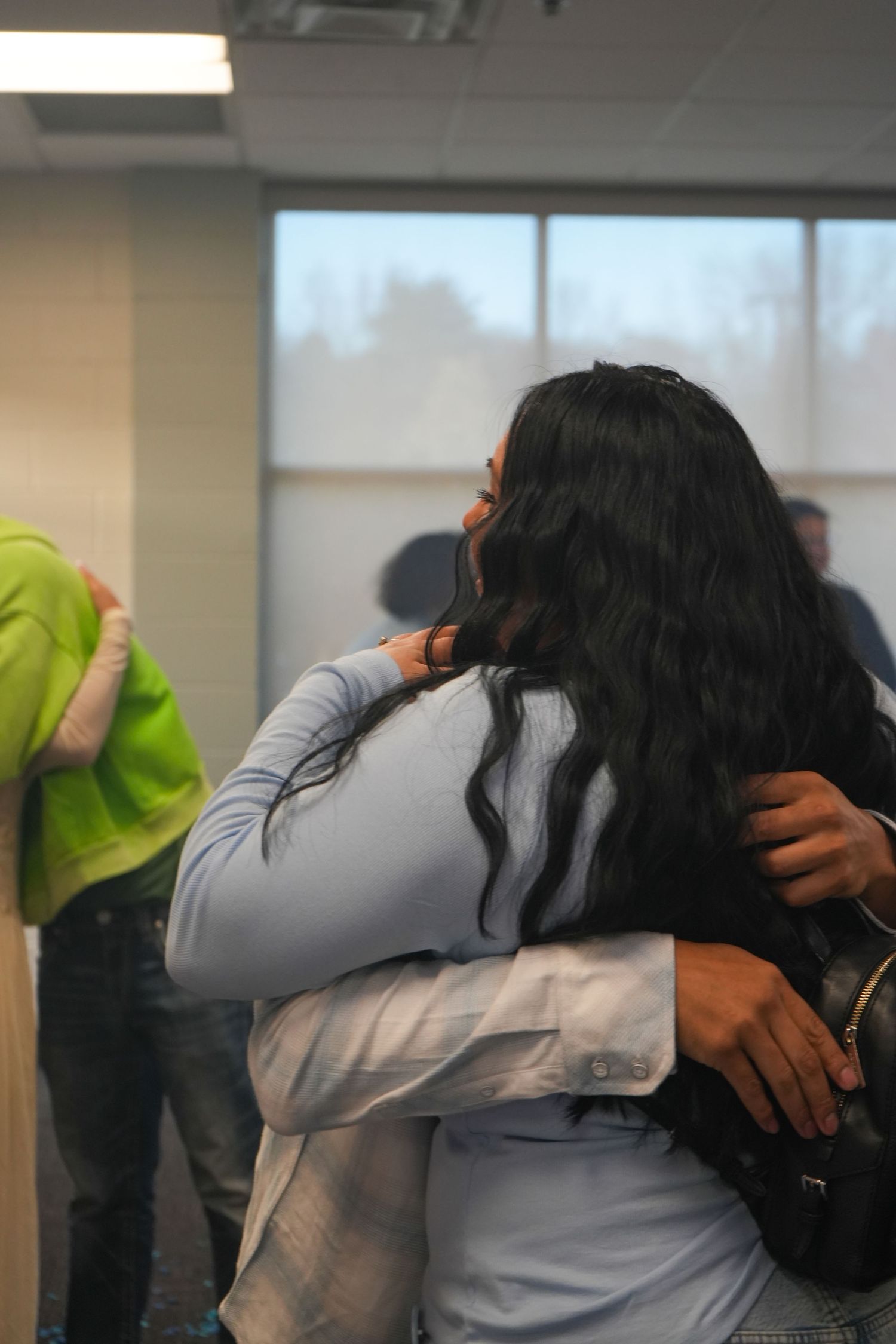 Two women sharing a warm embrace in an indoor setting, one with long black hair, another in a light blue top.