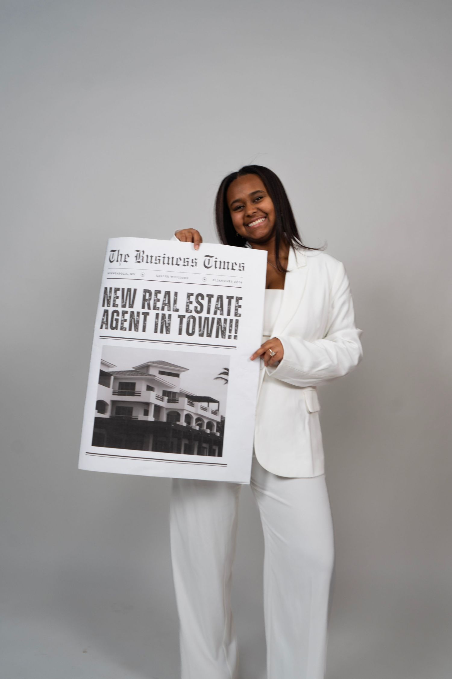 Smiling woman in white suit holding a large newspaper reading New Real Estate Agent in Town from The Business Times.