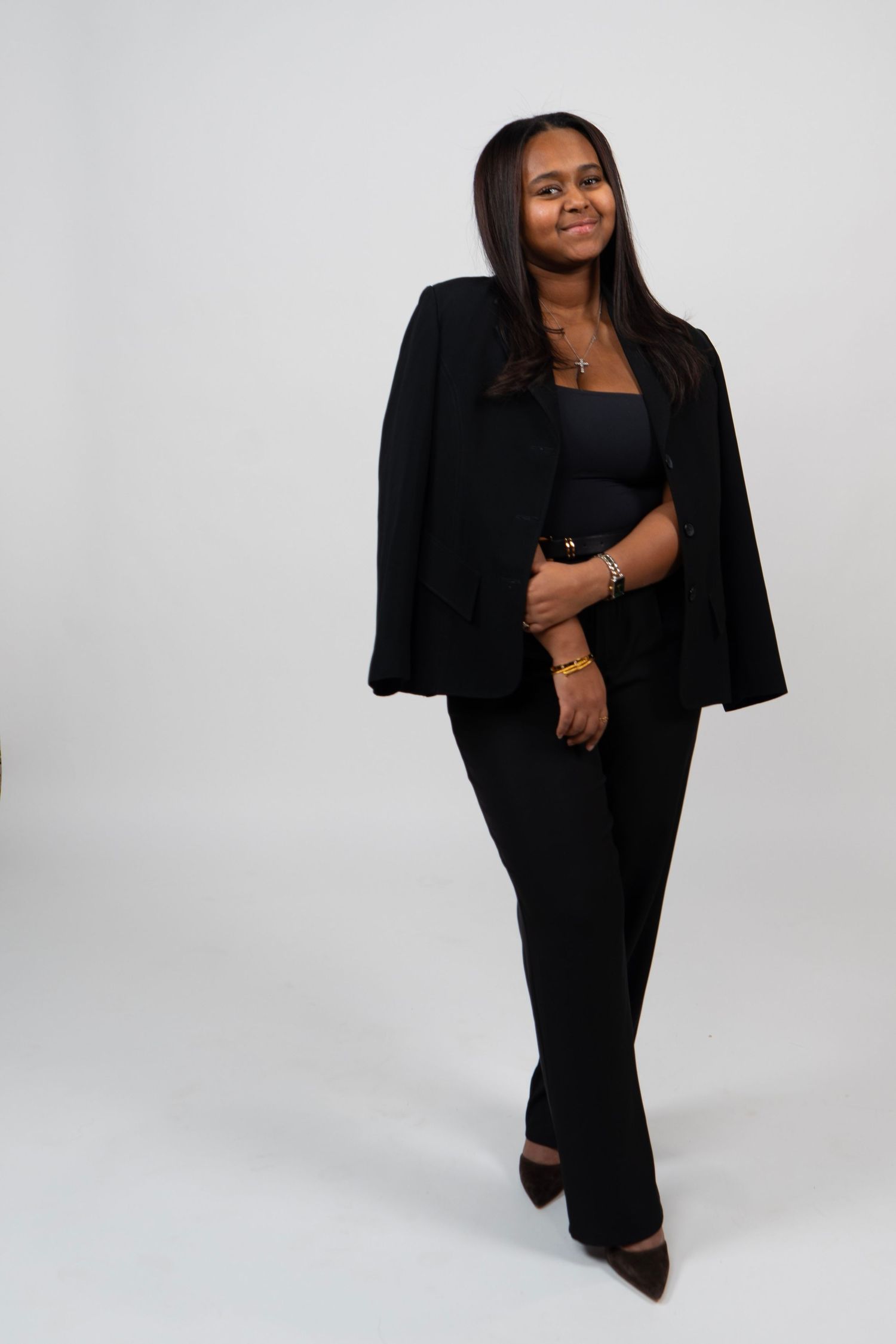 Young woman in all-black outfit with blazer cape, posing confidently against white background.
