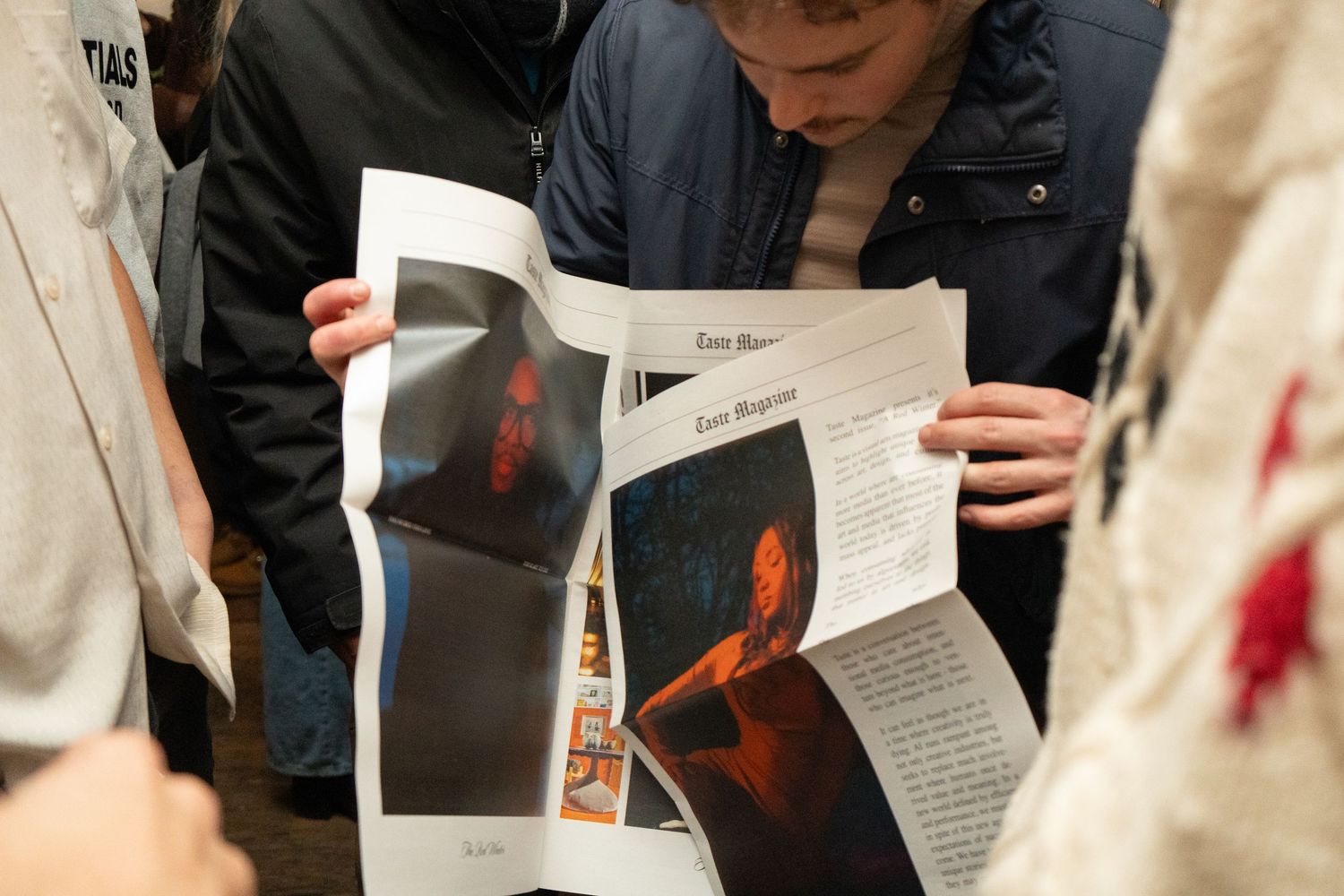 People gathered around reading a magazine featuring dark dramatic portrait photography at an indoor event.