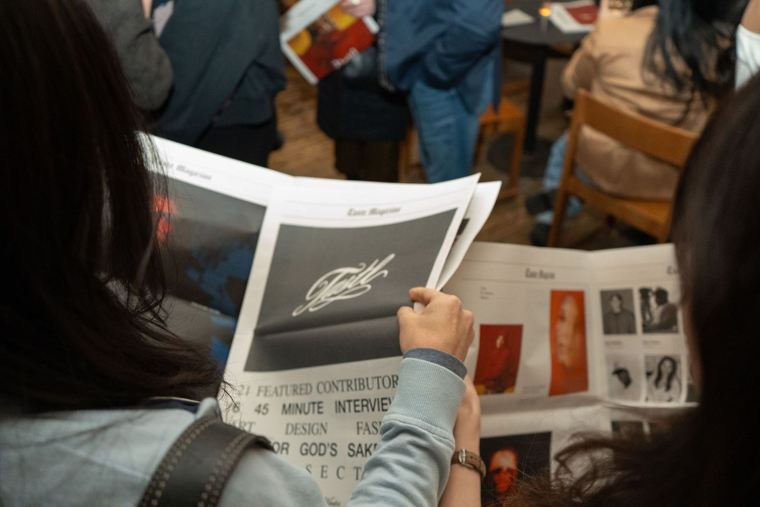 Person reading a magazine or program booklet at a crowded indoor event, with others visible in the background.
