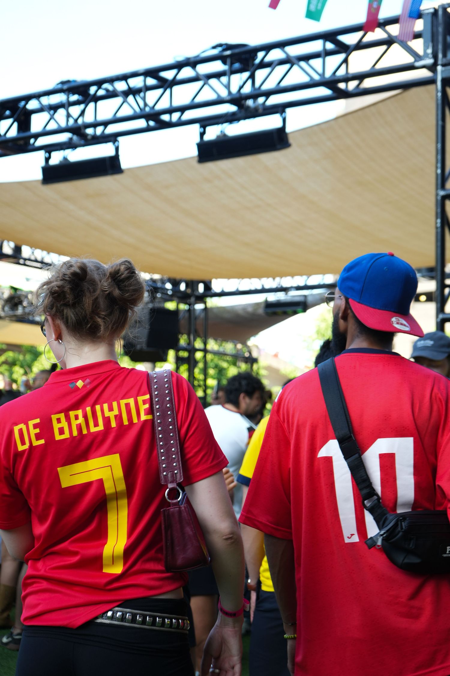 Two Belgian football fans wearing red De Bruyne number 7 and number 10 jerseys at an outdoor fan zone event.