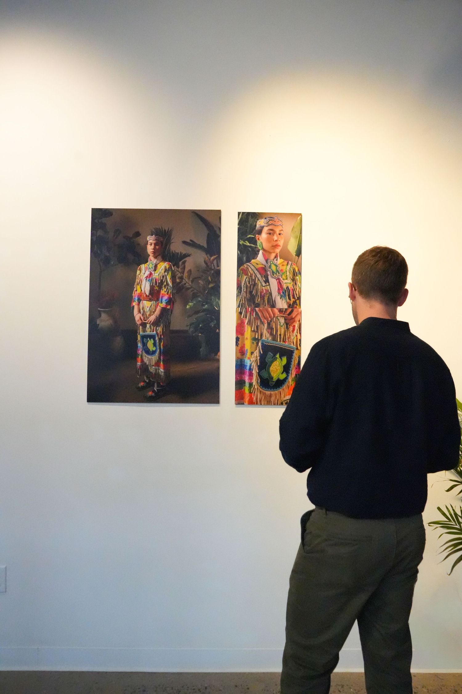 Man viewing colorful portrait photographs of women in traditional attire displayed on a white gallery wall.