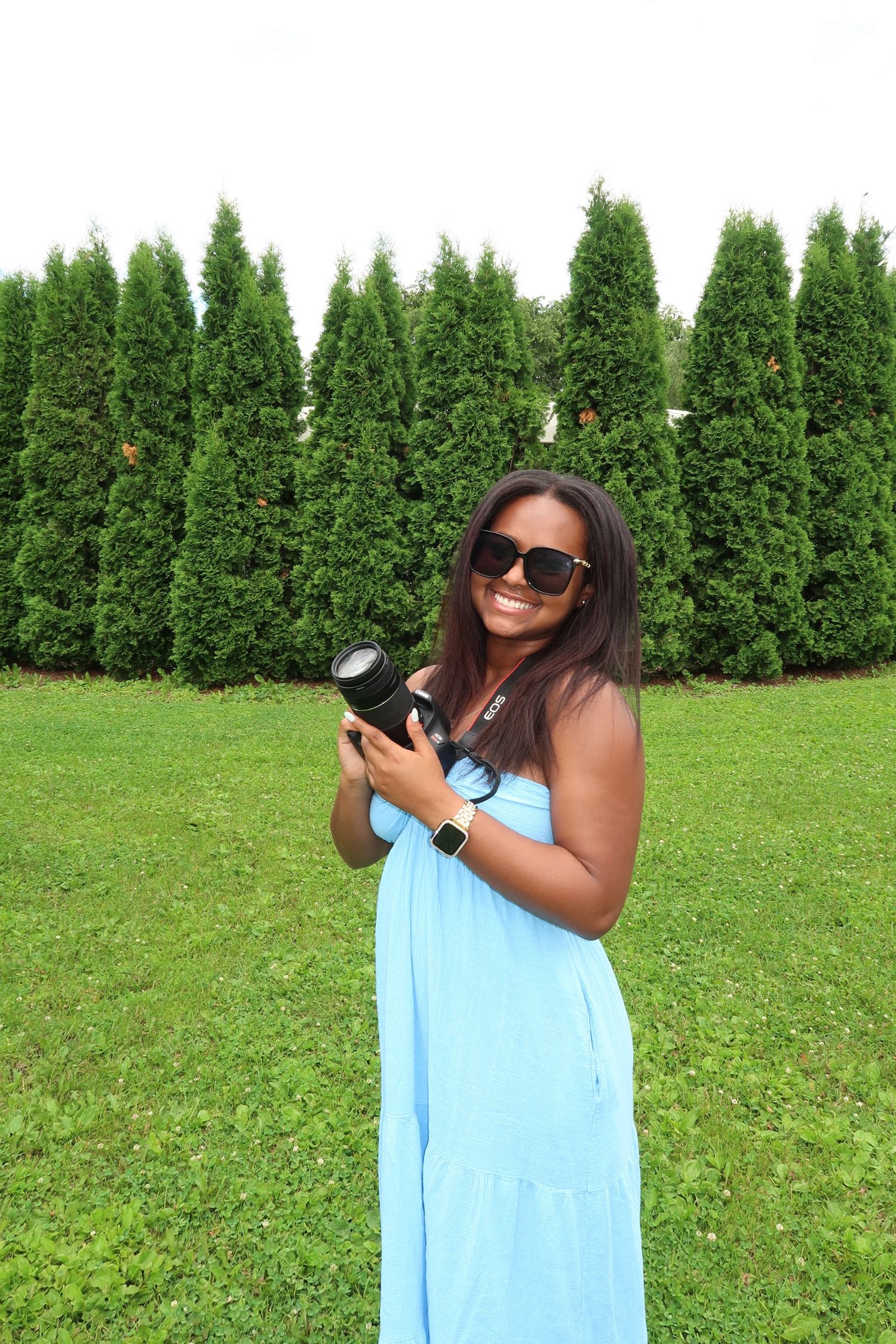 A bright turquoise outfit contrasts with a row of green cypress trees in a garden setting.