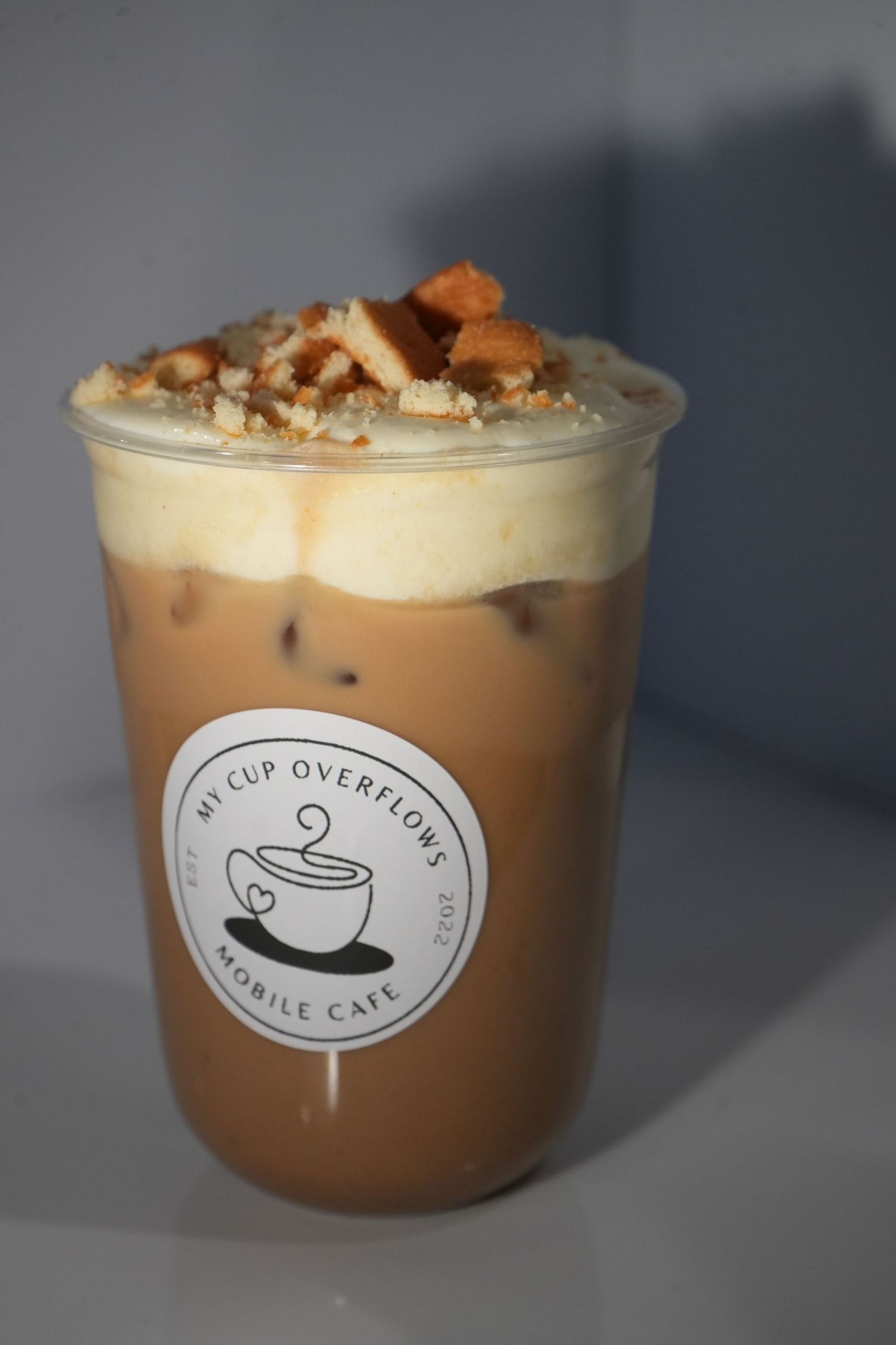 Iced coffee drink with cream topping and cookie crumbles in a branded My Cup Overflows Mobile Cafe cup.