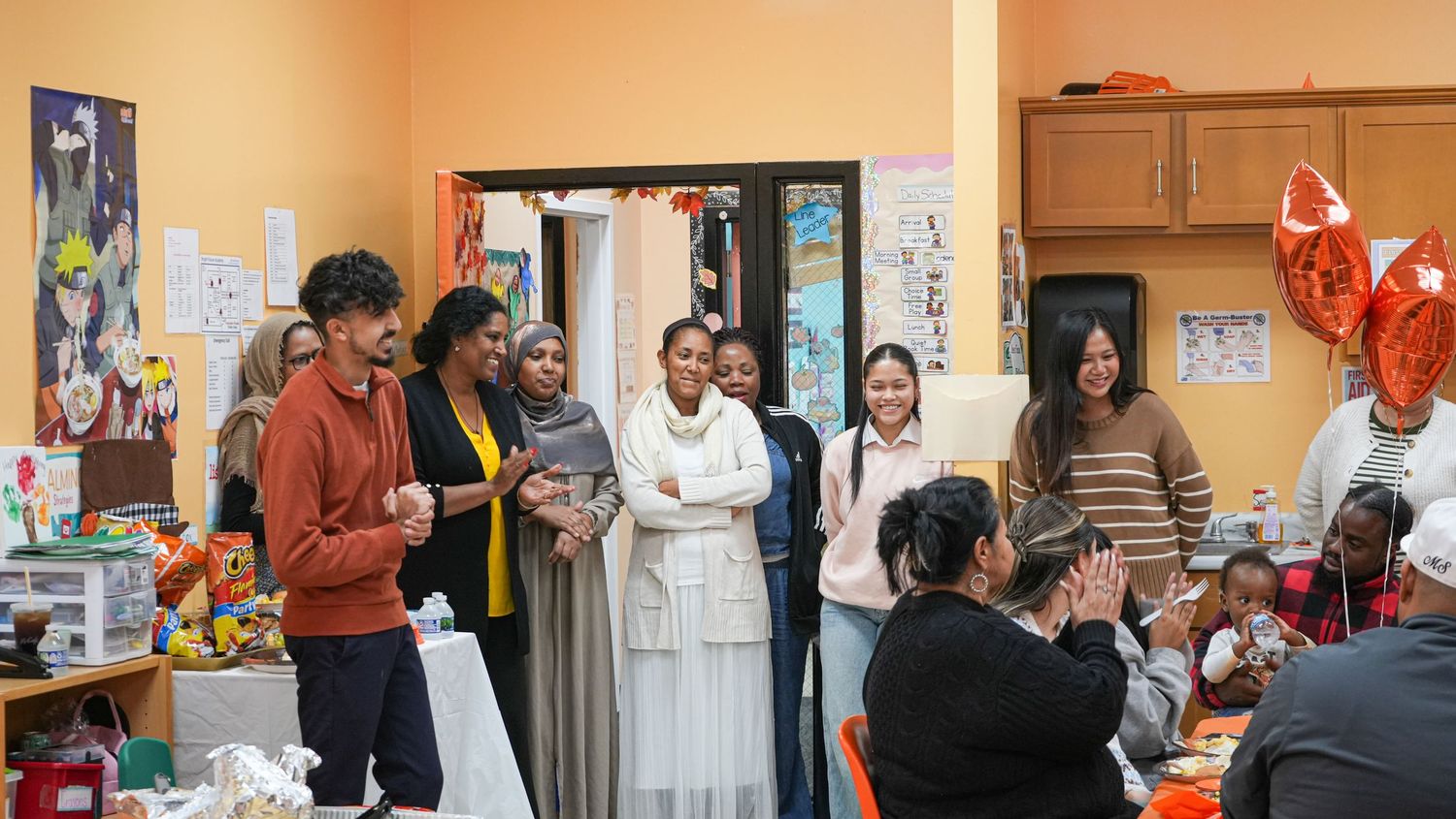Group of diverse people gathered in a colorful community center room for a social event with balloons.