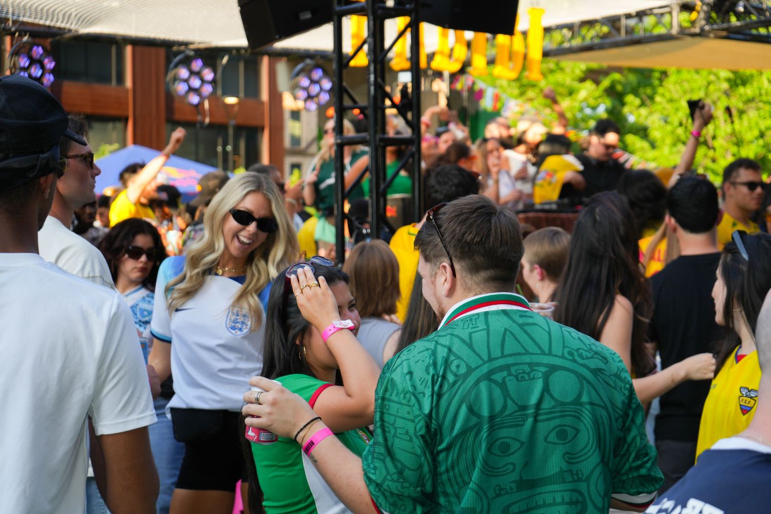 Crowd of sports fans in yellow and green gather outdoors at a lively fan event on a sunny day.