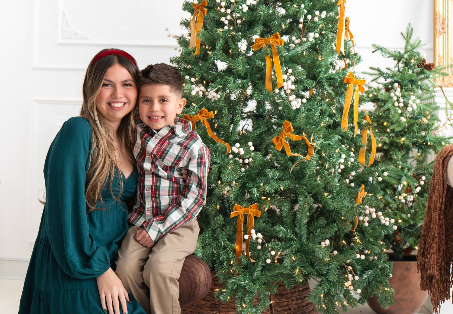 Woman and young boy smiling together in front of decorated Christmas tree with gold ribbons.