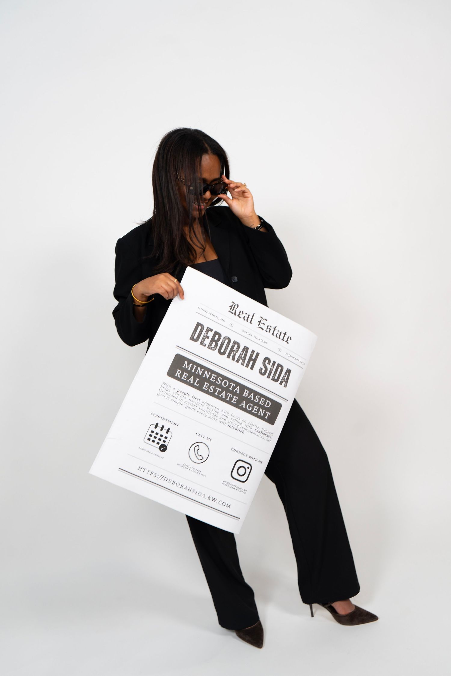 Minnesota-based real estate agent Deborah Sida poses in black suit holding oversized newspaper advertisement.