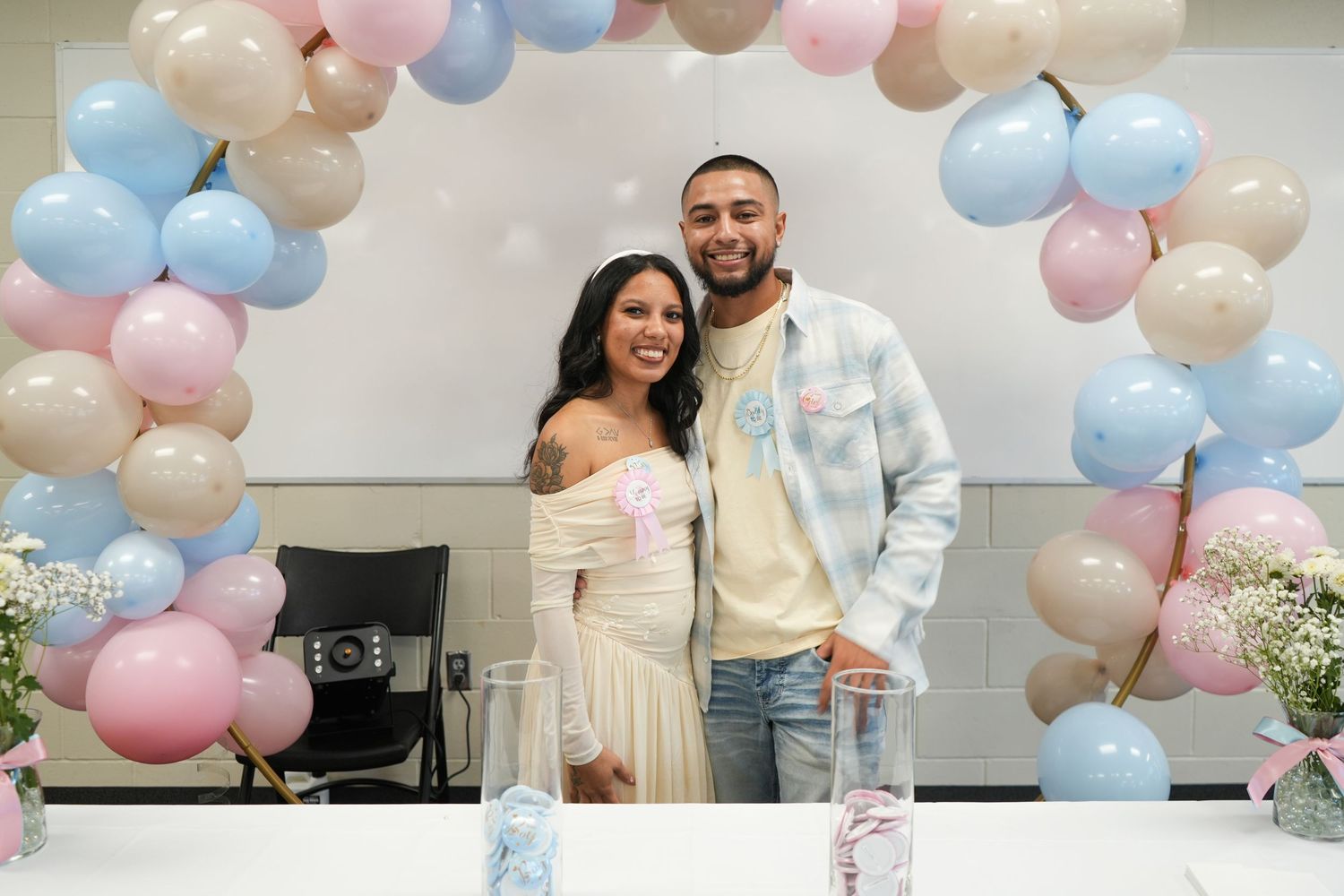 Couple smiling at a gender reveal party with pink and blue balloon arch decoration.