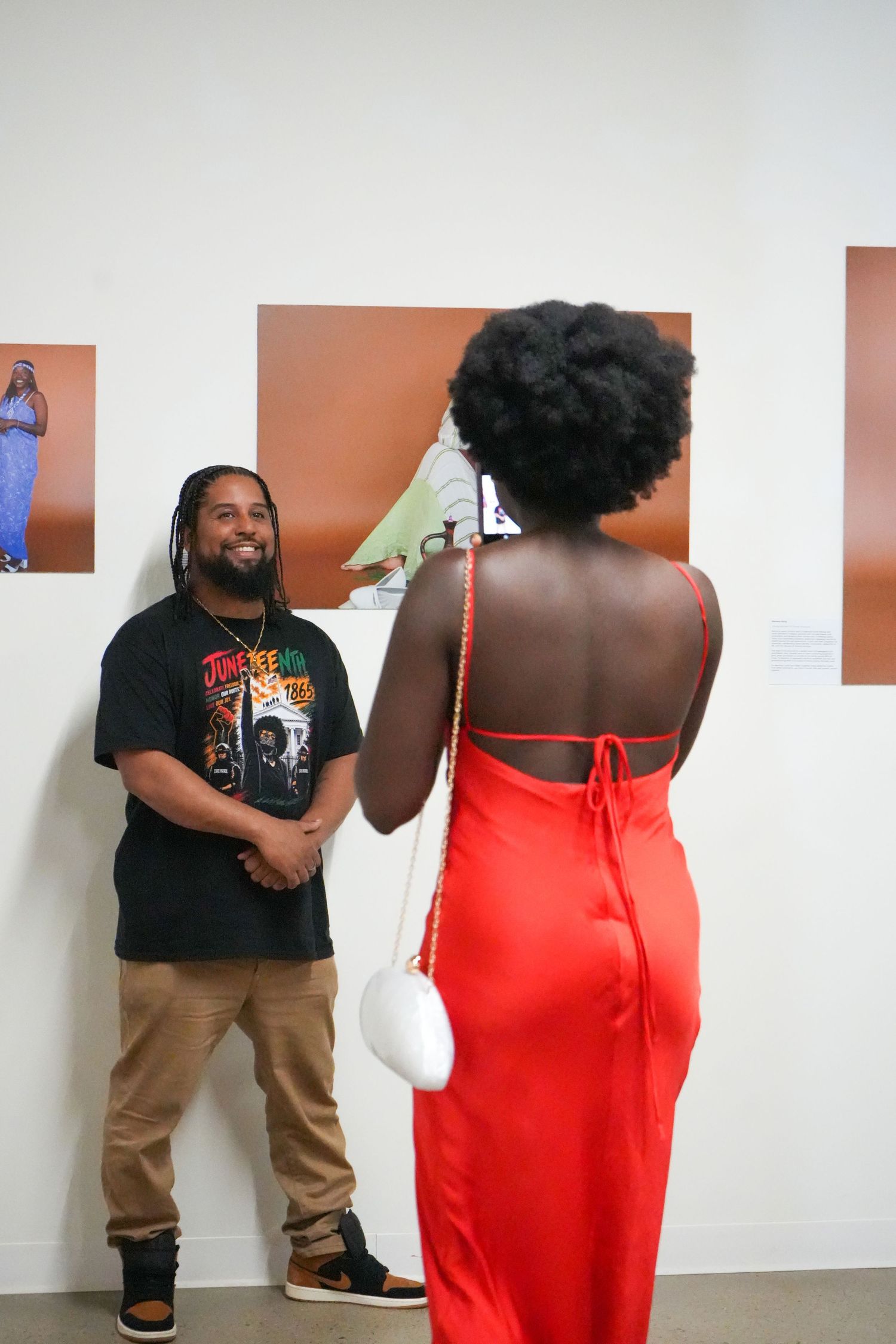 Man in black graphic tee chats with woman in red backless dress at an art gallery exhibition.