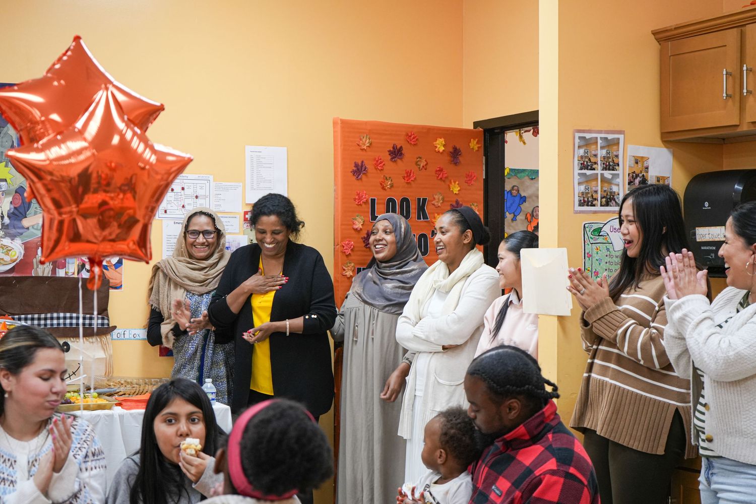 Diverse group of women celebrating at a party with orange star balloon, food table, and festive decorations indoors.