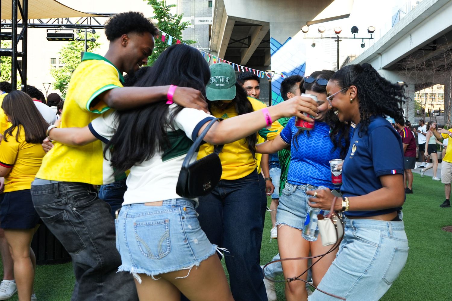 Group of young people hugging and celebrating outdoors at a lively event, wearing colorful summer outfits.