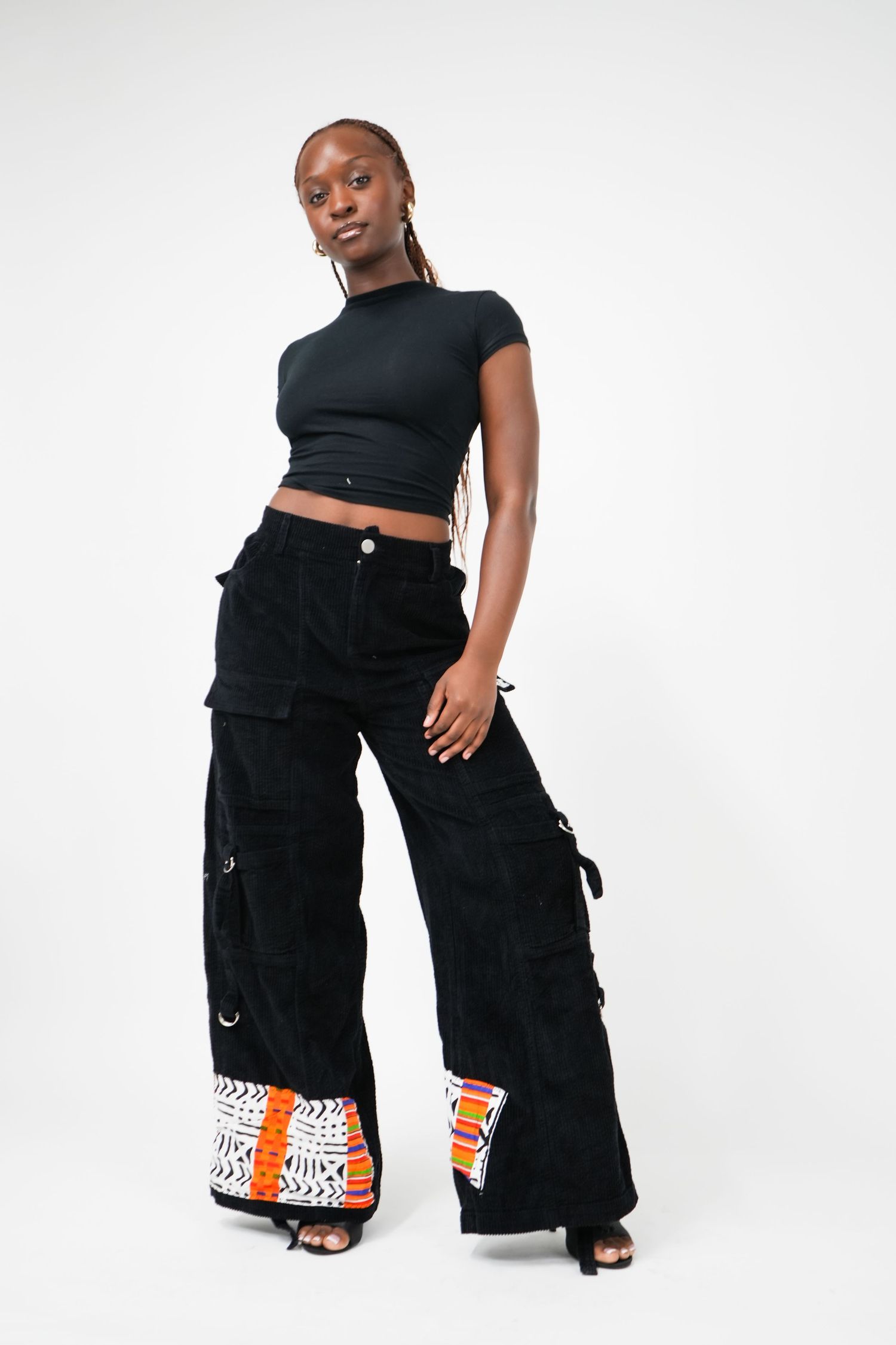 Woman wearing black crop top and wide-leg black cargo pants with colorful patchwork hem detail, studio shot.