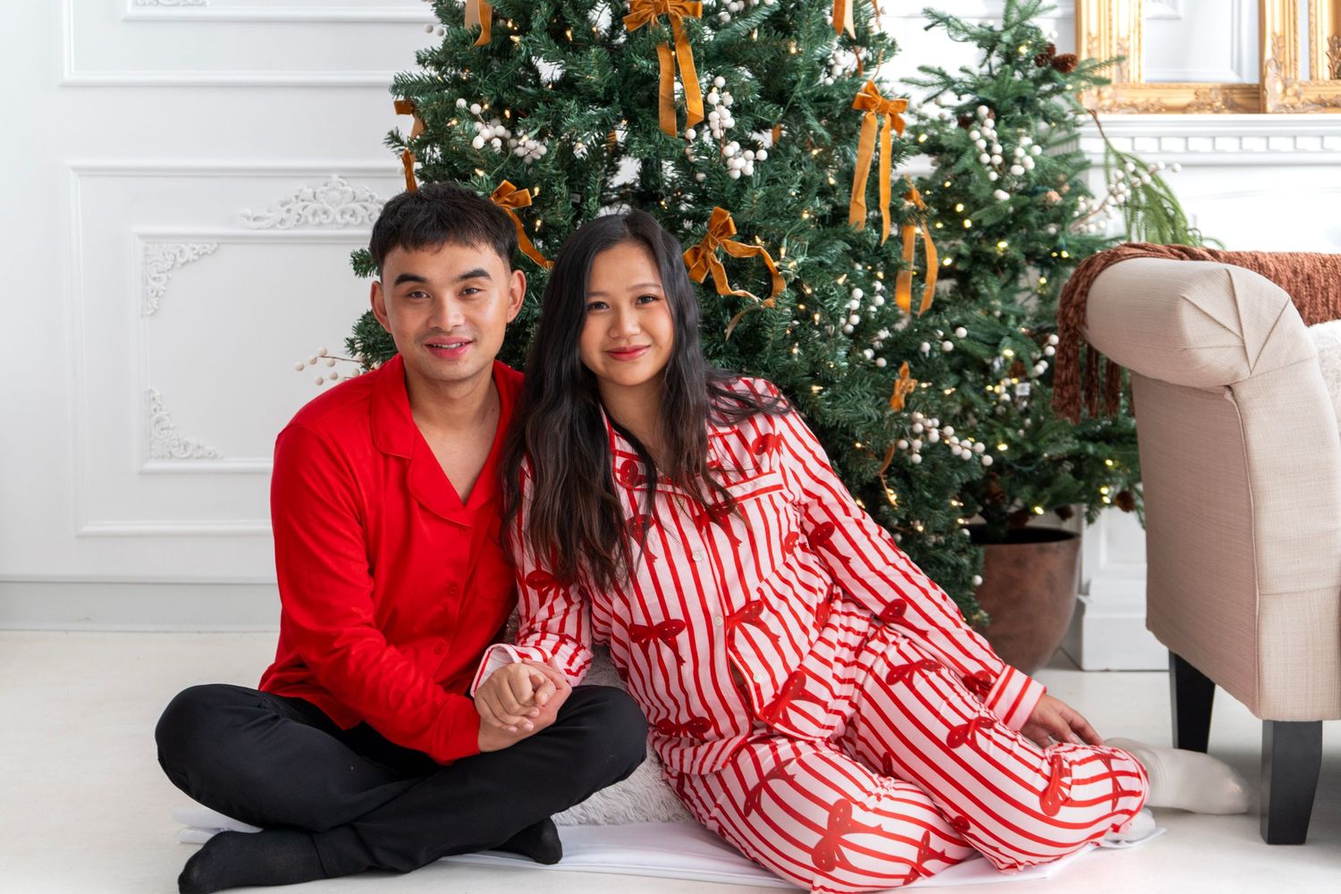 Couple in matching red and white striped pajamas sitting together in front of a decorated Christmas tree.
