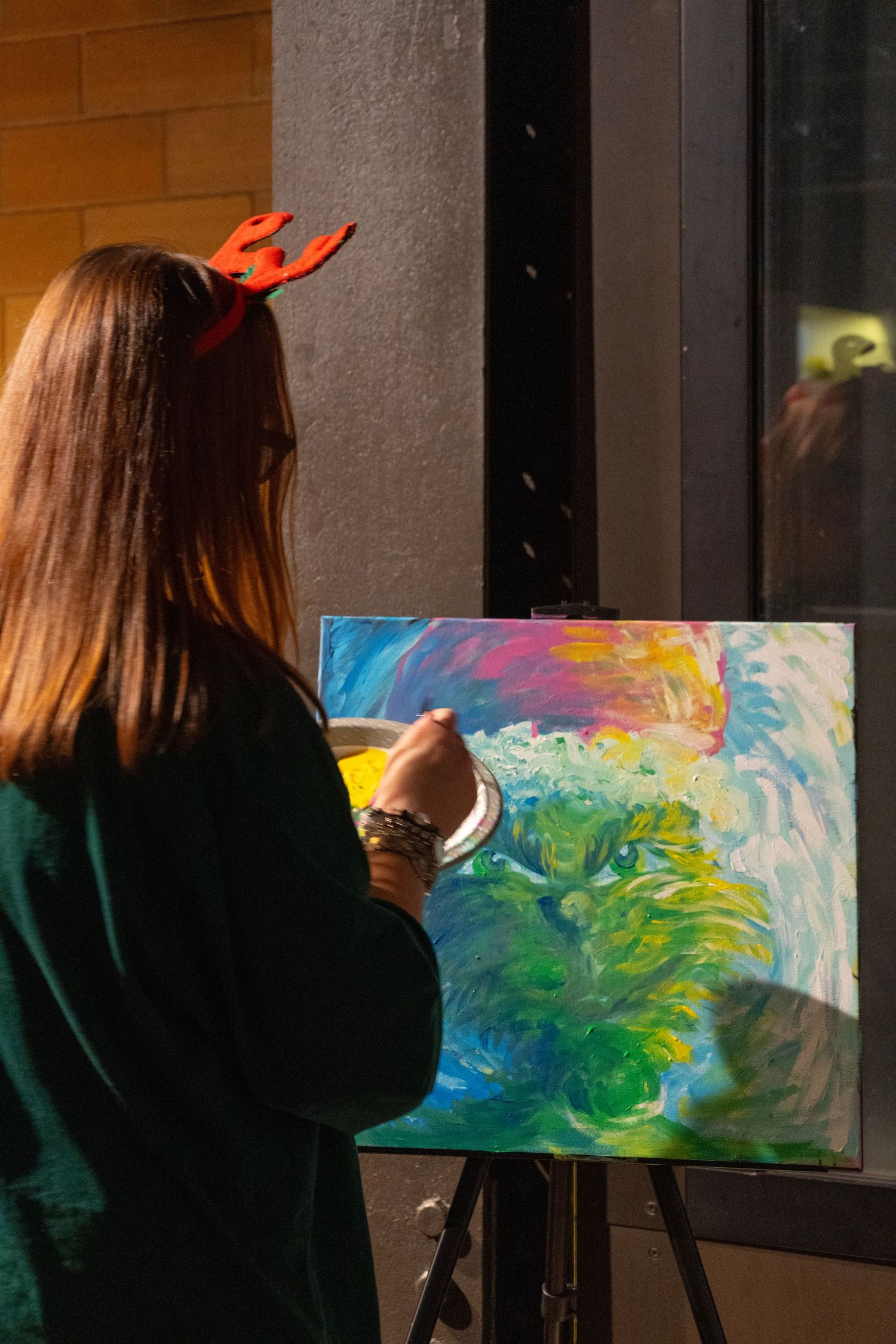 Woman with reindeer antlers headband painting colorful abstract art on canvas easel outdoors.
