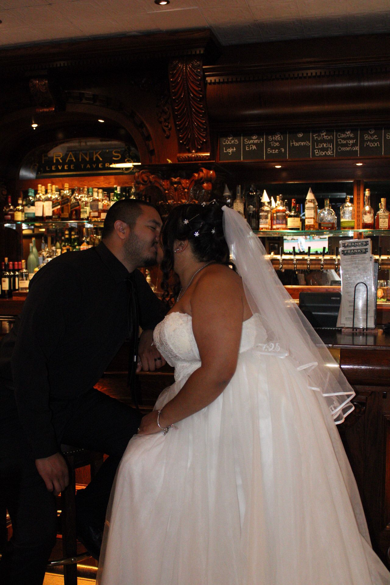 Bride and groom sharing a kiss at a bar wedding reception, bride wearing white gown and veil.