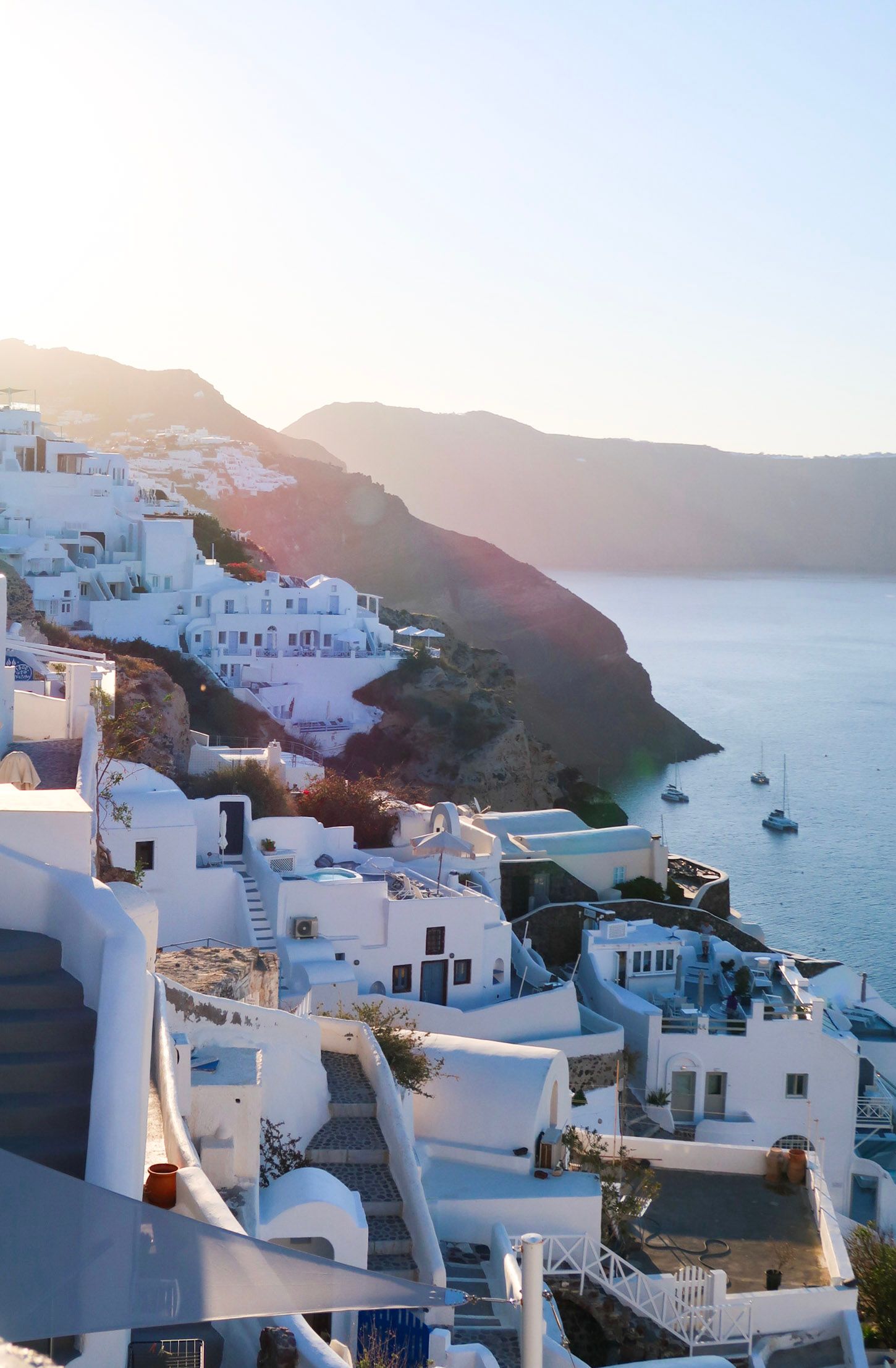 Whitewashed buildings cascade down Santorini cliffs overlooking the caldera at golden sunset in Greece.